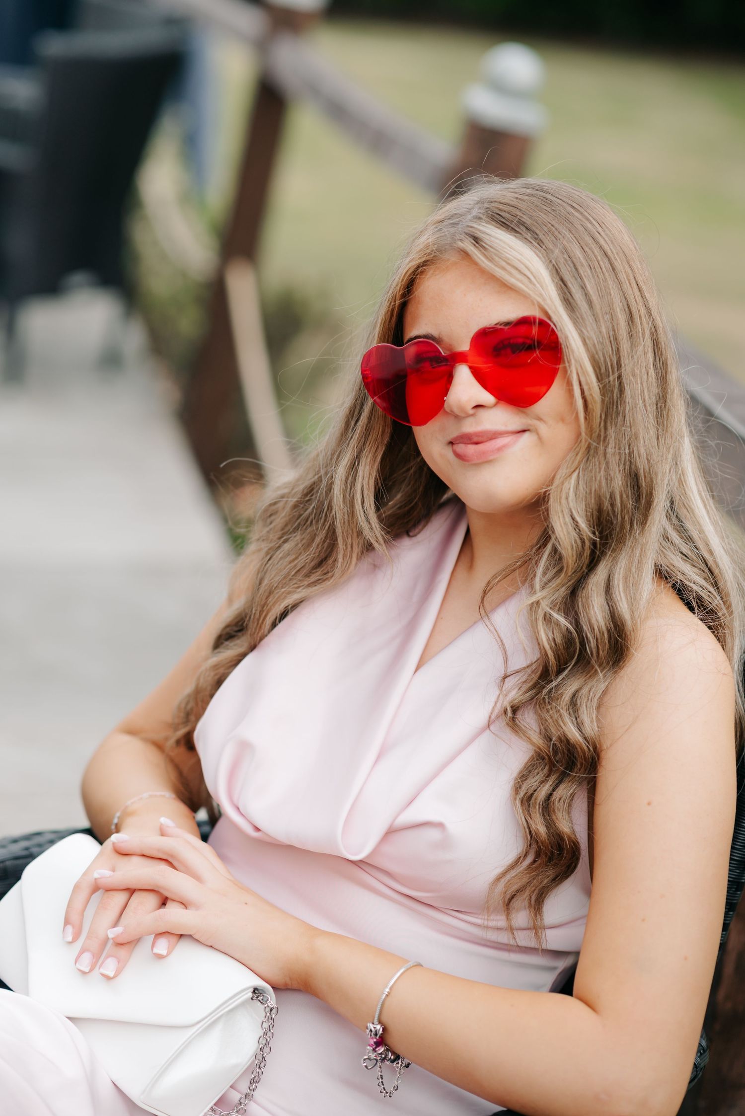 A woman in a pink top and red heart-shaped sunglasses poses outdoors in a series of casual portraits.