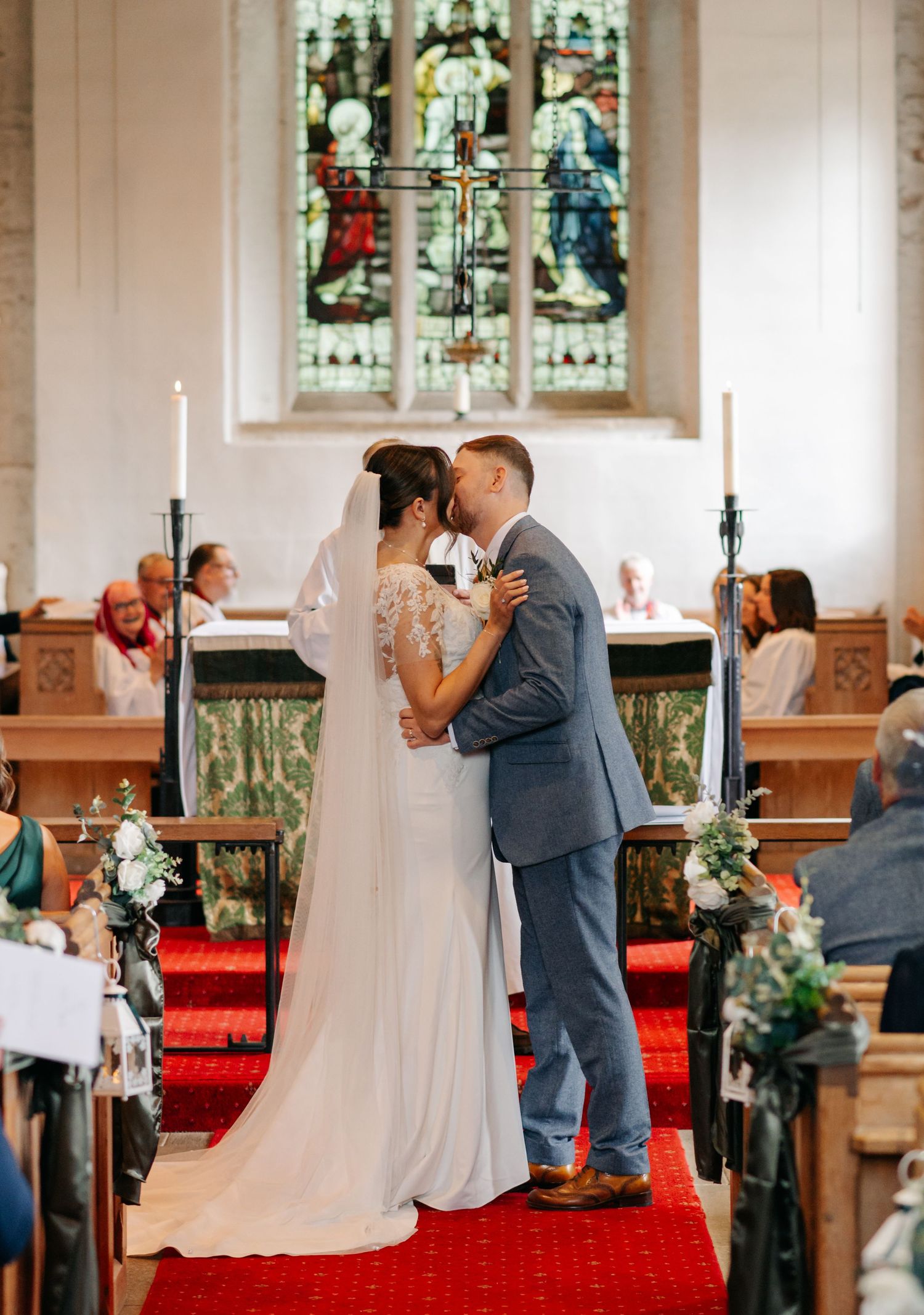 A wedding ceremony taking place in a church with stained glass windows and red carpet.