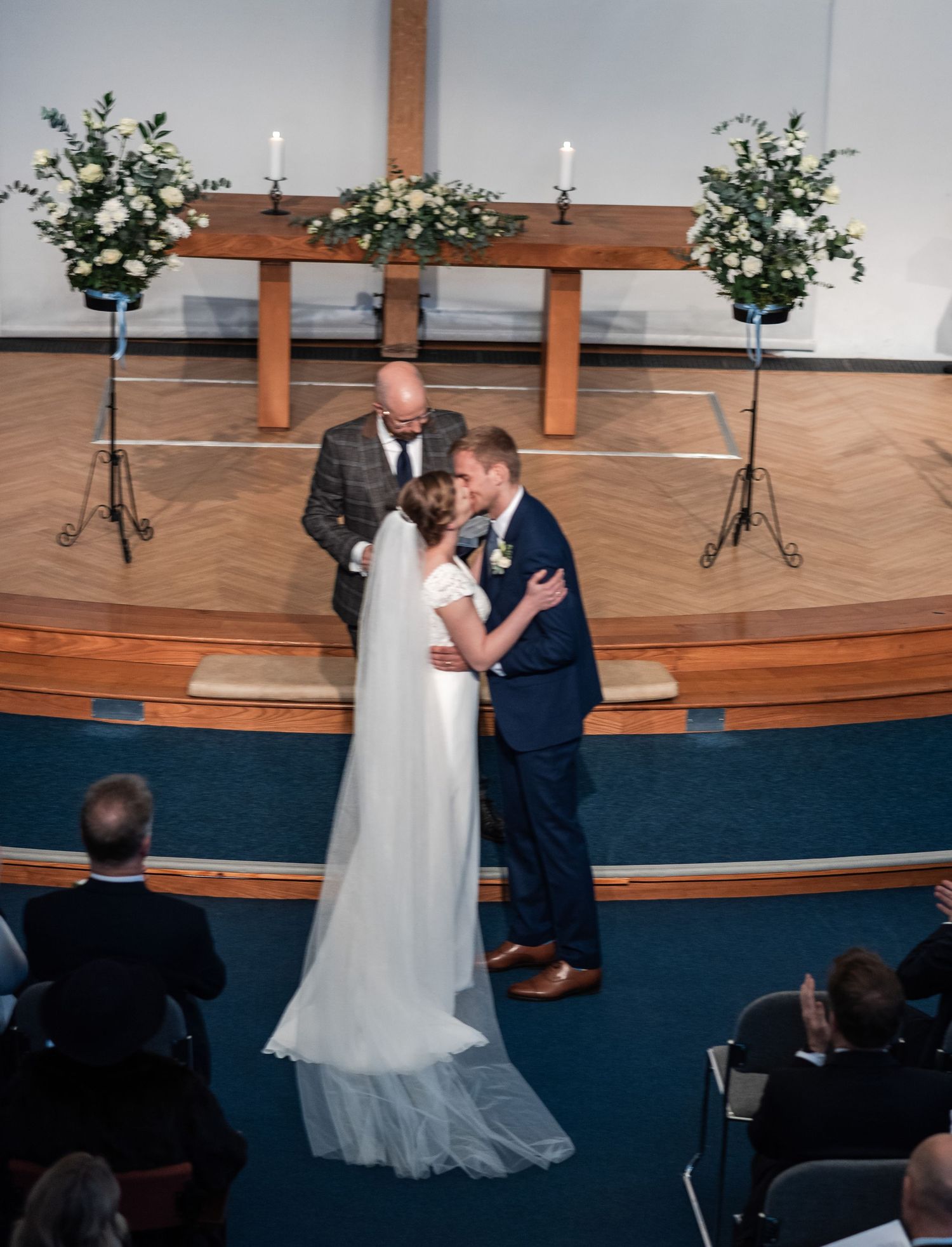 Wedding ceremony in a church sanctuary with wooden stage and blue accents.