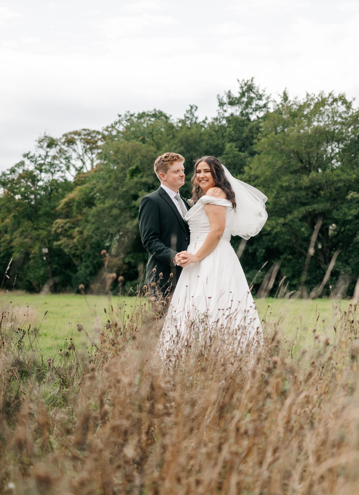 A romantic wedding photo taken in a field of tall grass with trees in the background.