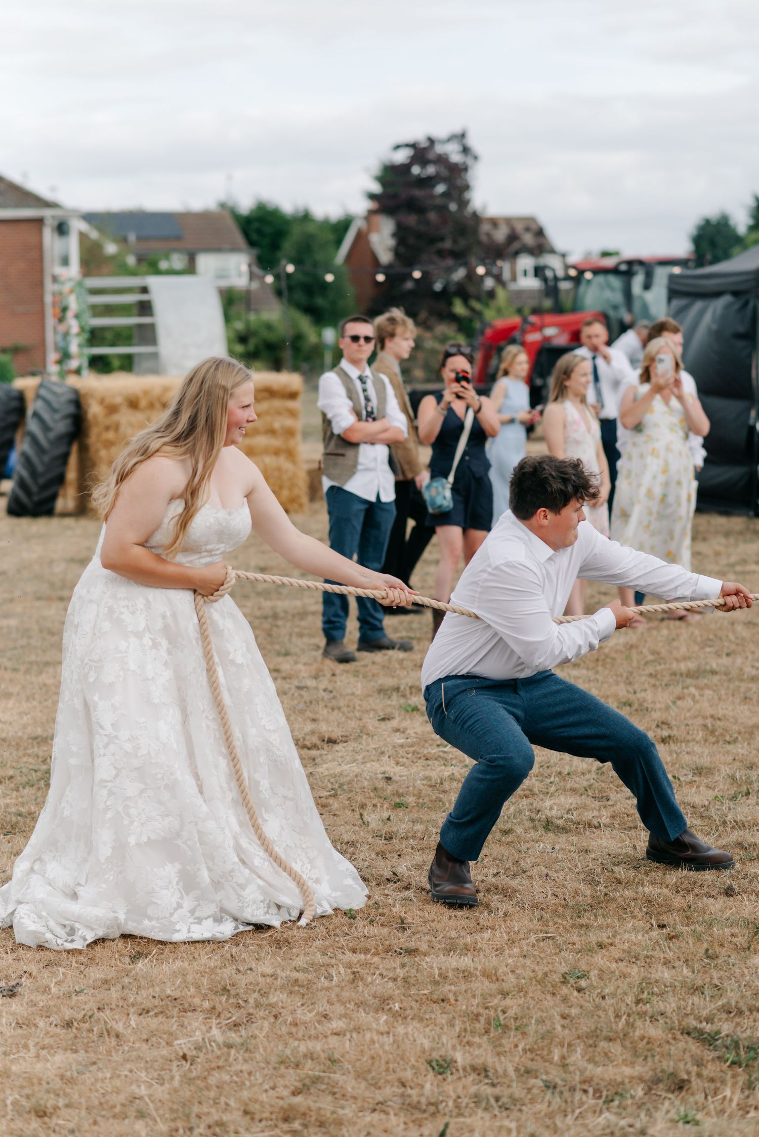 A group playing tug of war outdoors with wedding attire and casual clothes.