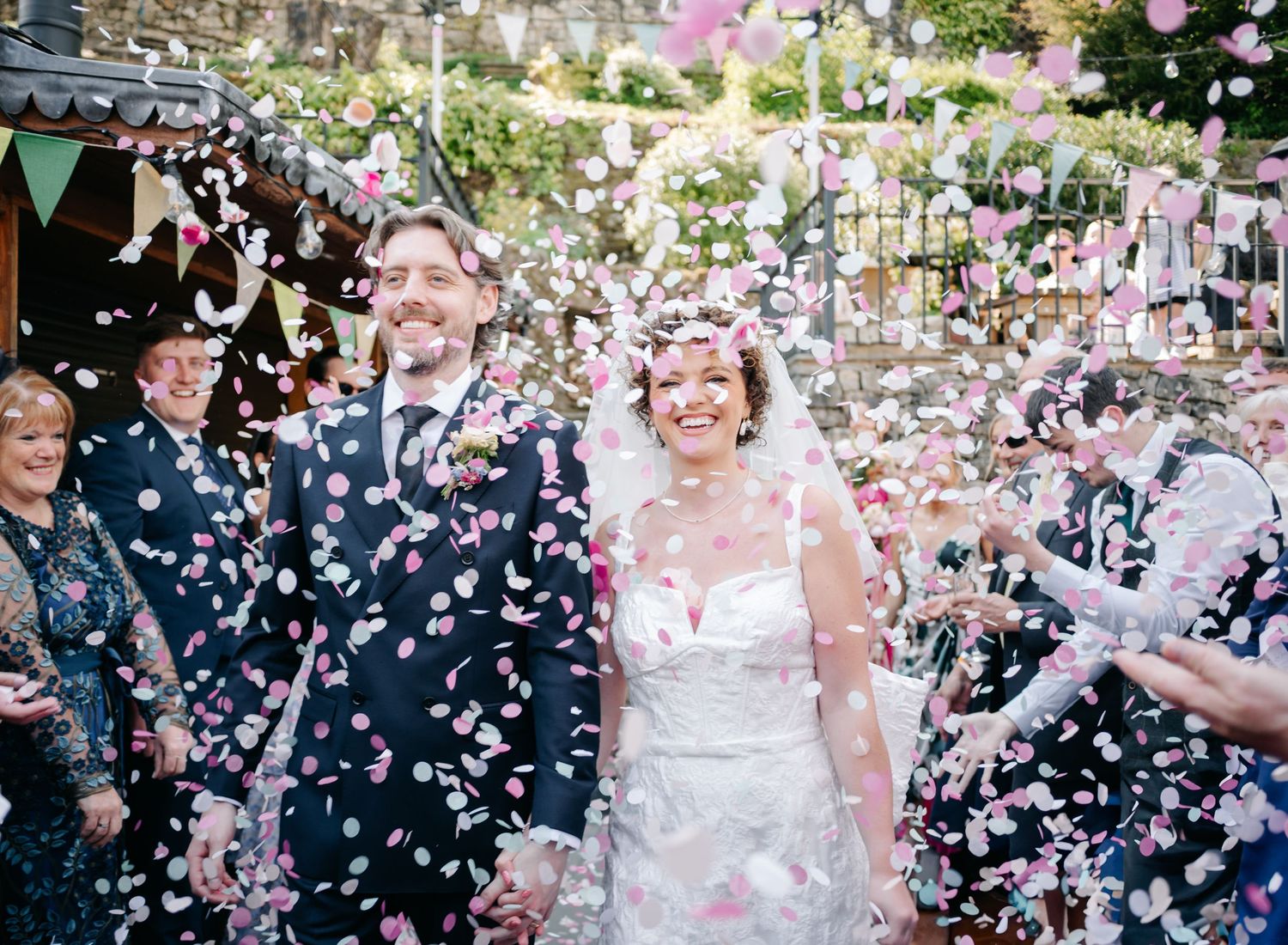 Newlyweds walk through a shower of white flower petals as wedding guests celebrate their exit from the ceremony.