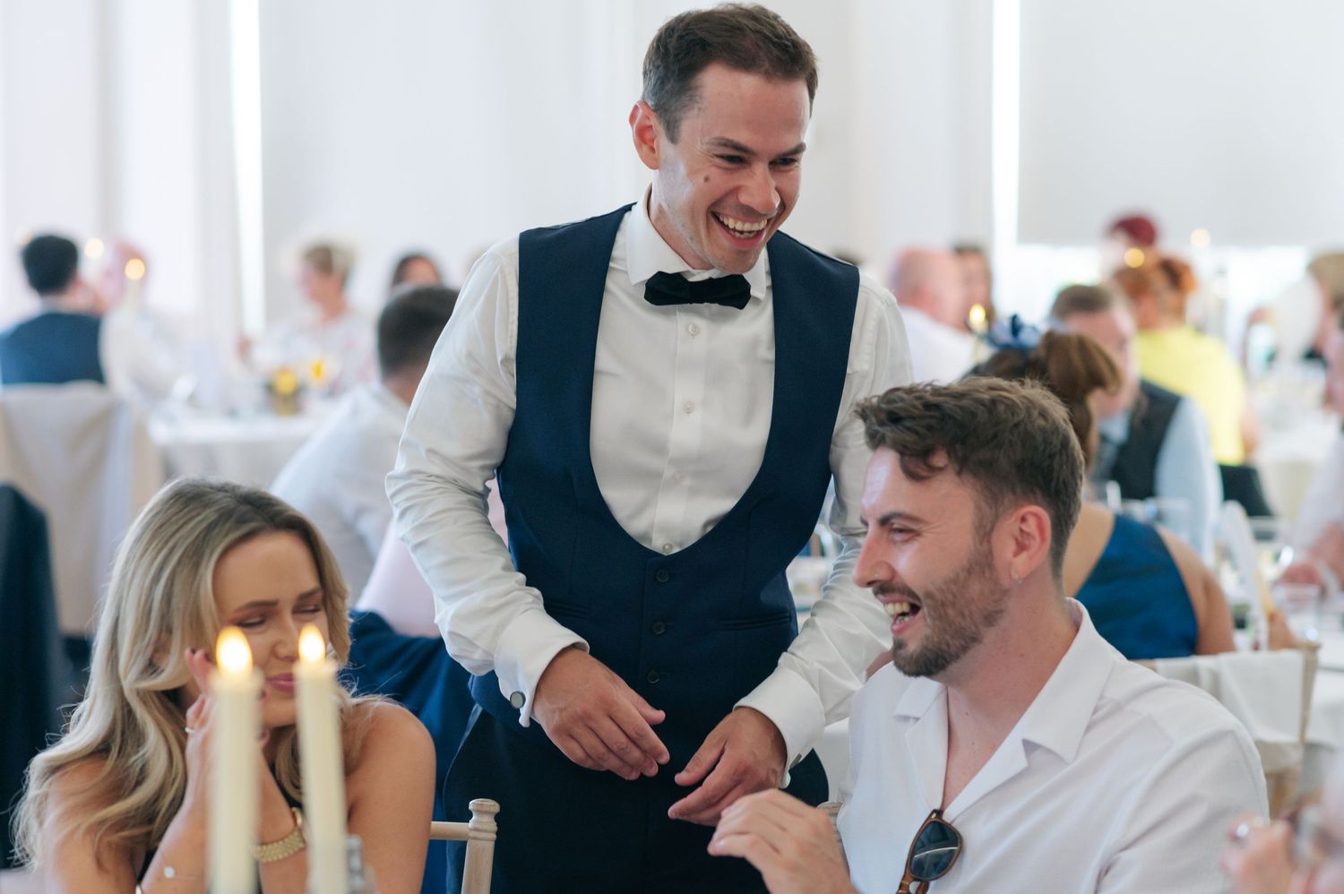 Wedding reception guests laughing and enjoying themselves at decorated indoor venue.