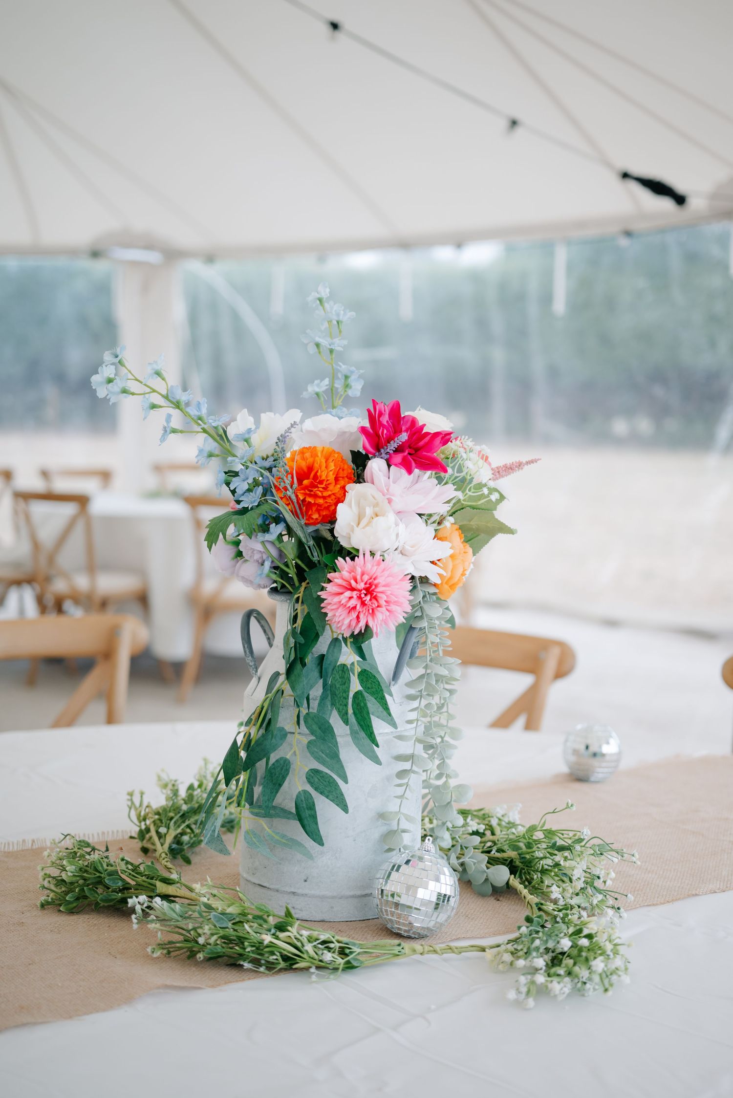 Elegant wedding table centerpieces featuring pink and orange dahlias with eucalyptus in glass vases on burlap runners.