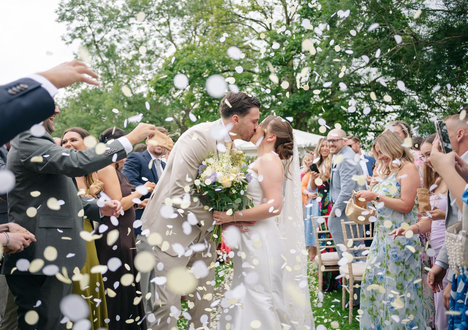 Wedding guests throw white confetti in celebration at an outdoor garden ceremony.