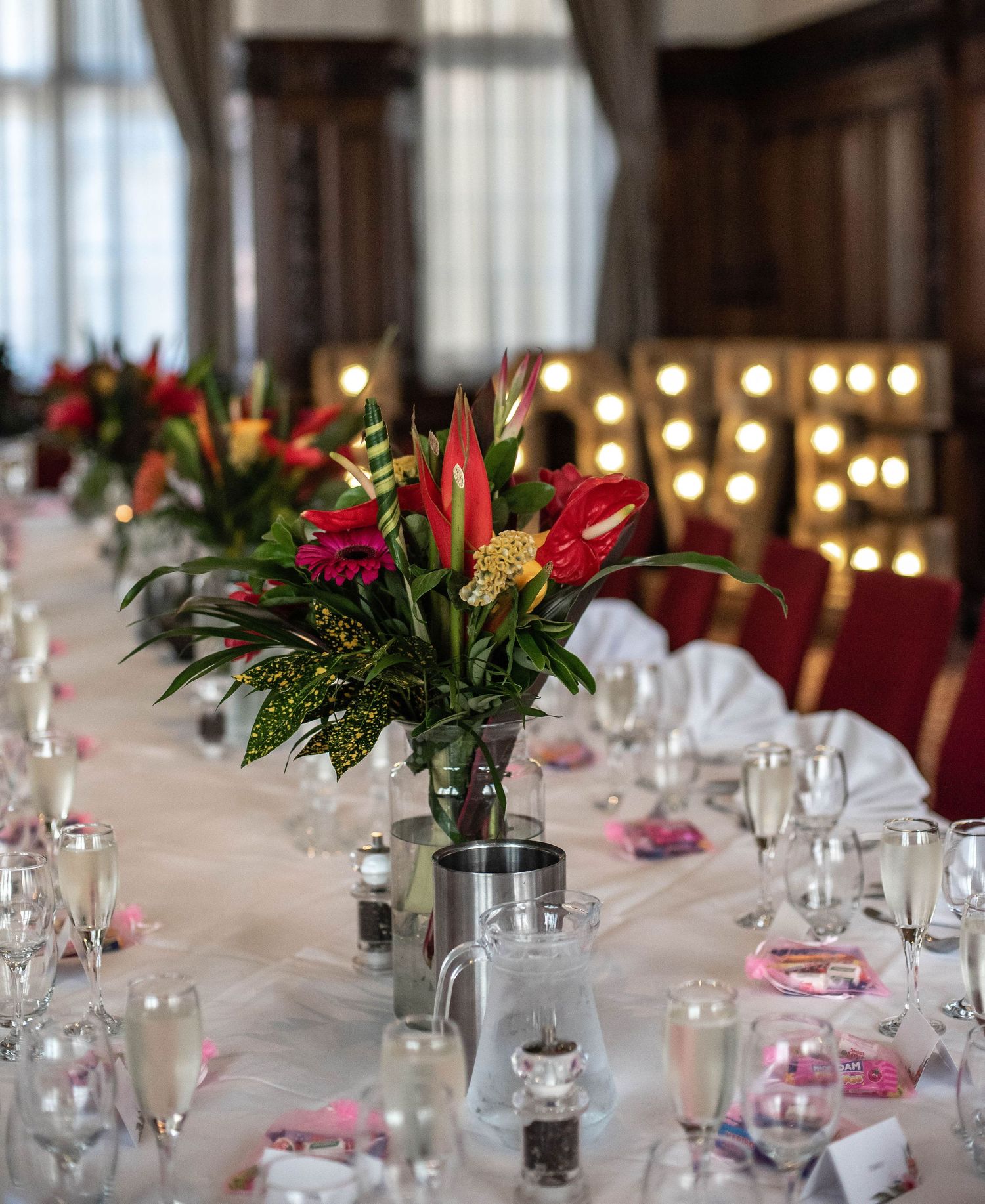Elegant wedding reception table with red floral centerpieces and glowing candles.