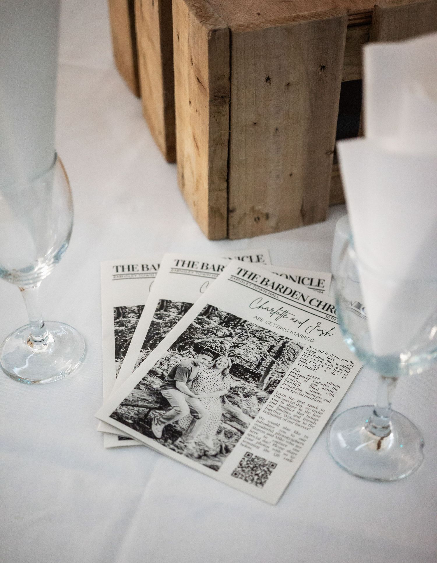 Wedding reception table setting with vintage newspaper programs and wine glasses.