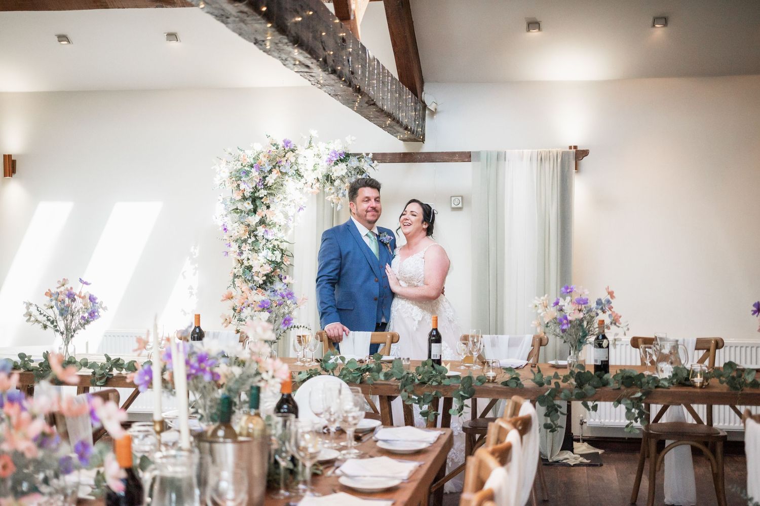 Elegant wedding reception setup with floral arch and rustic table settings in a bright venue.
