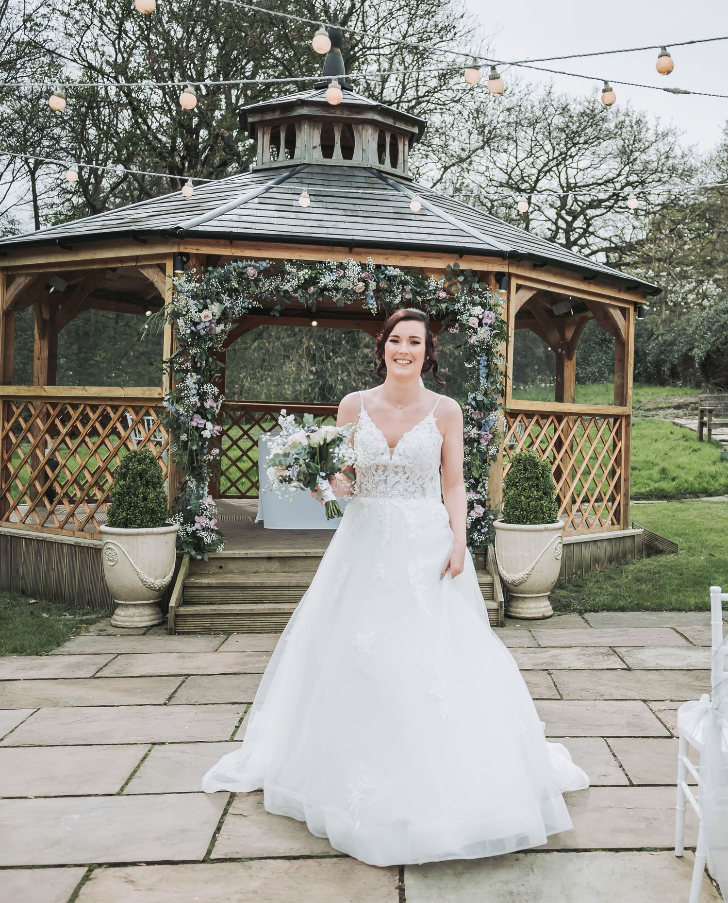 Beautiful wedding gazebo decorated with floral arrangements and string lights on stone patio.