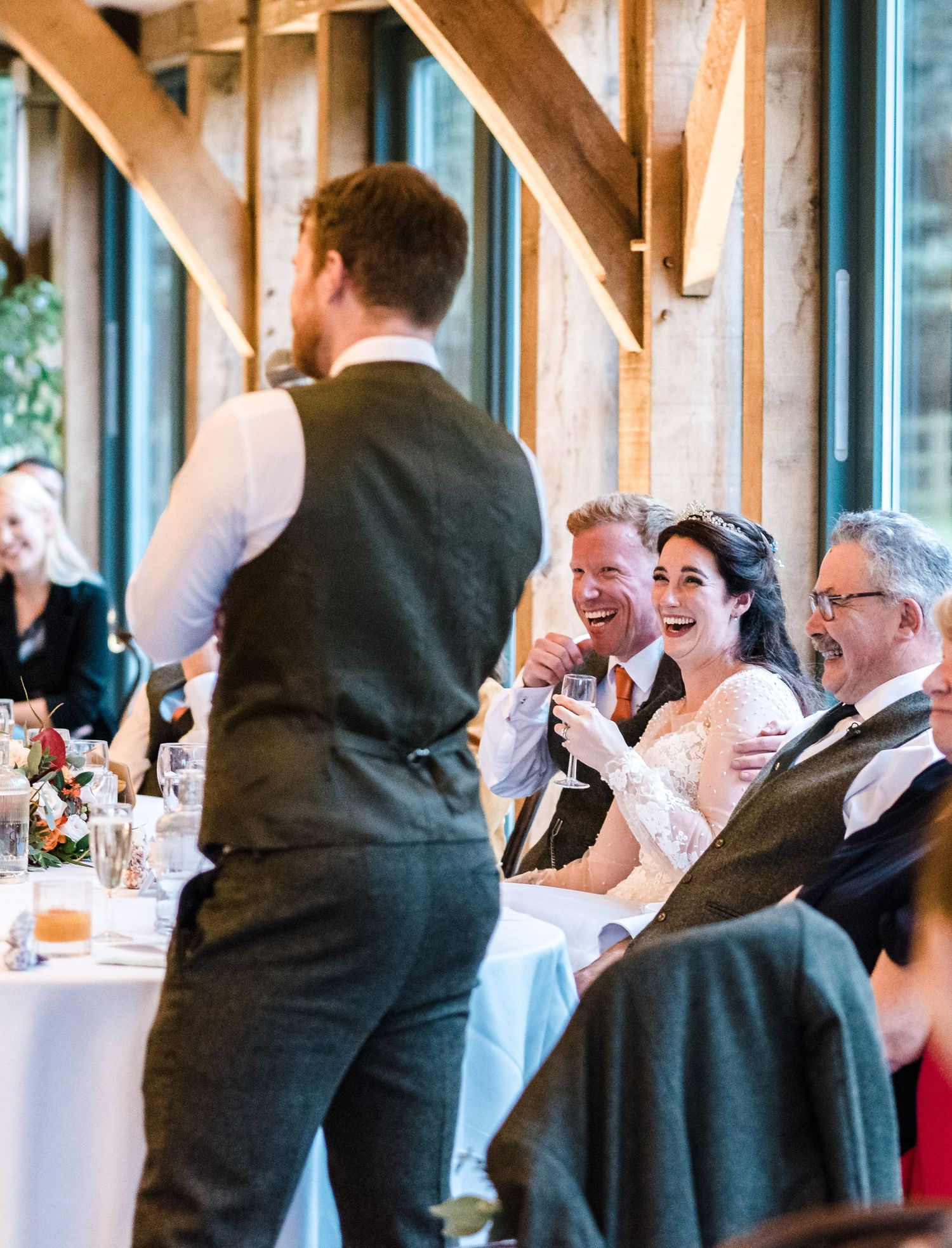 Speaker delivers wedding toast as guests laugh and enjoy the reception.