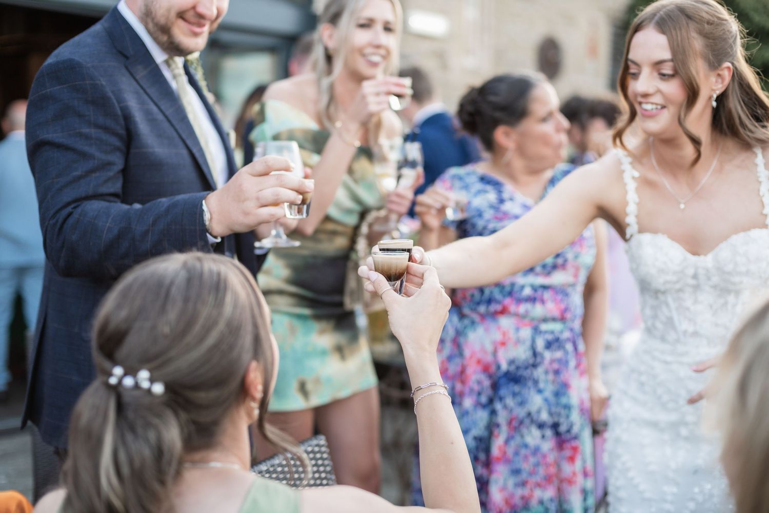 Wedding guests raise glasses in a celebratory toast outdoors.