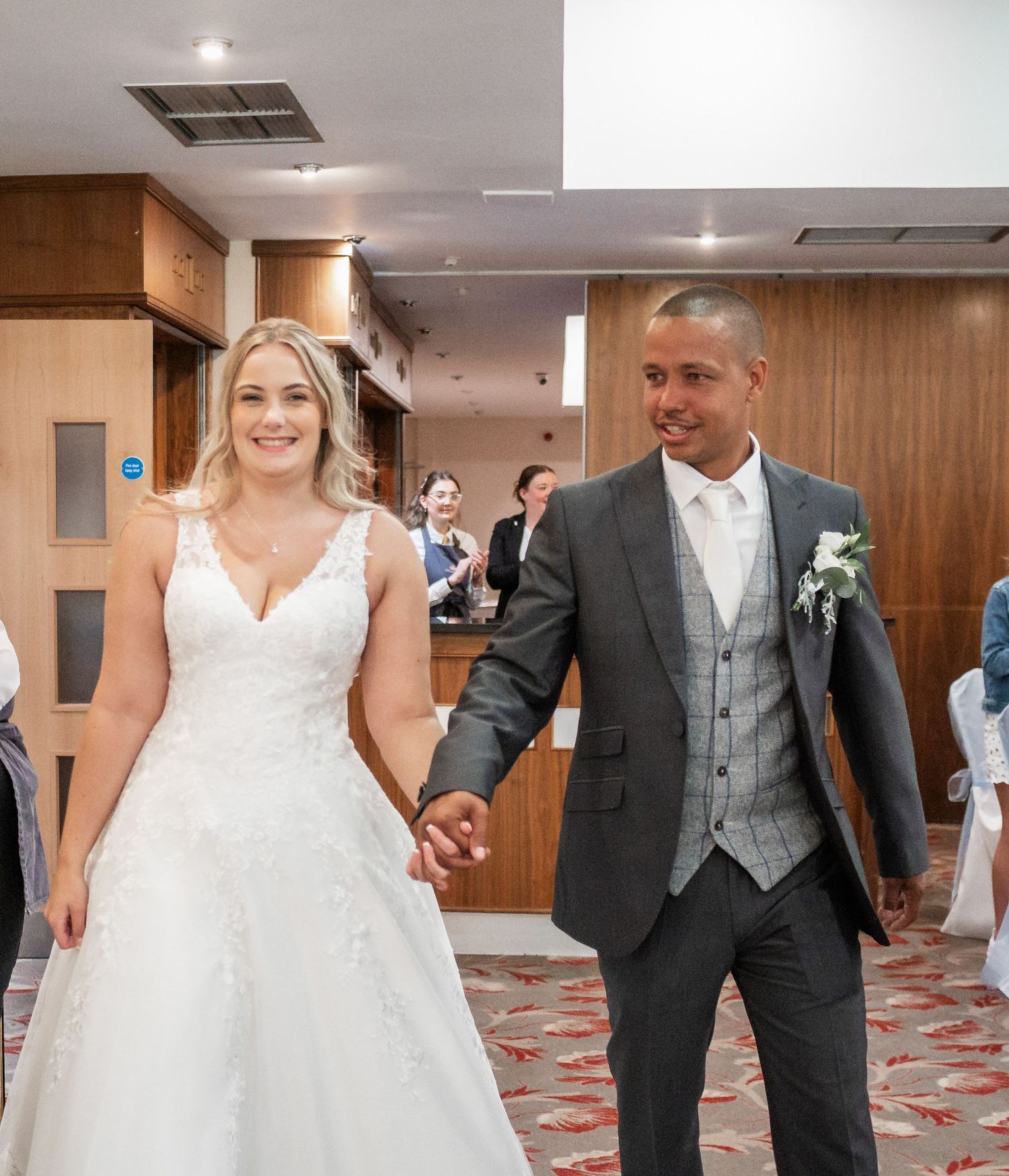 Newlyweds walk hand in hand through an indoor venue after their wedding ceremony.