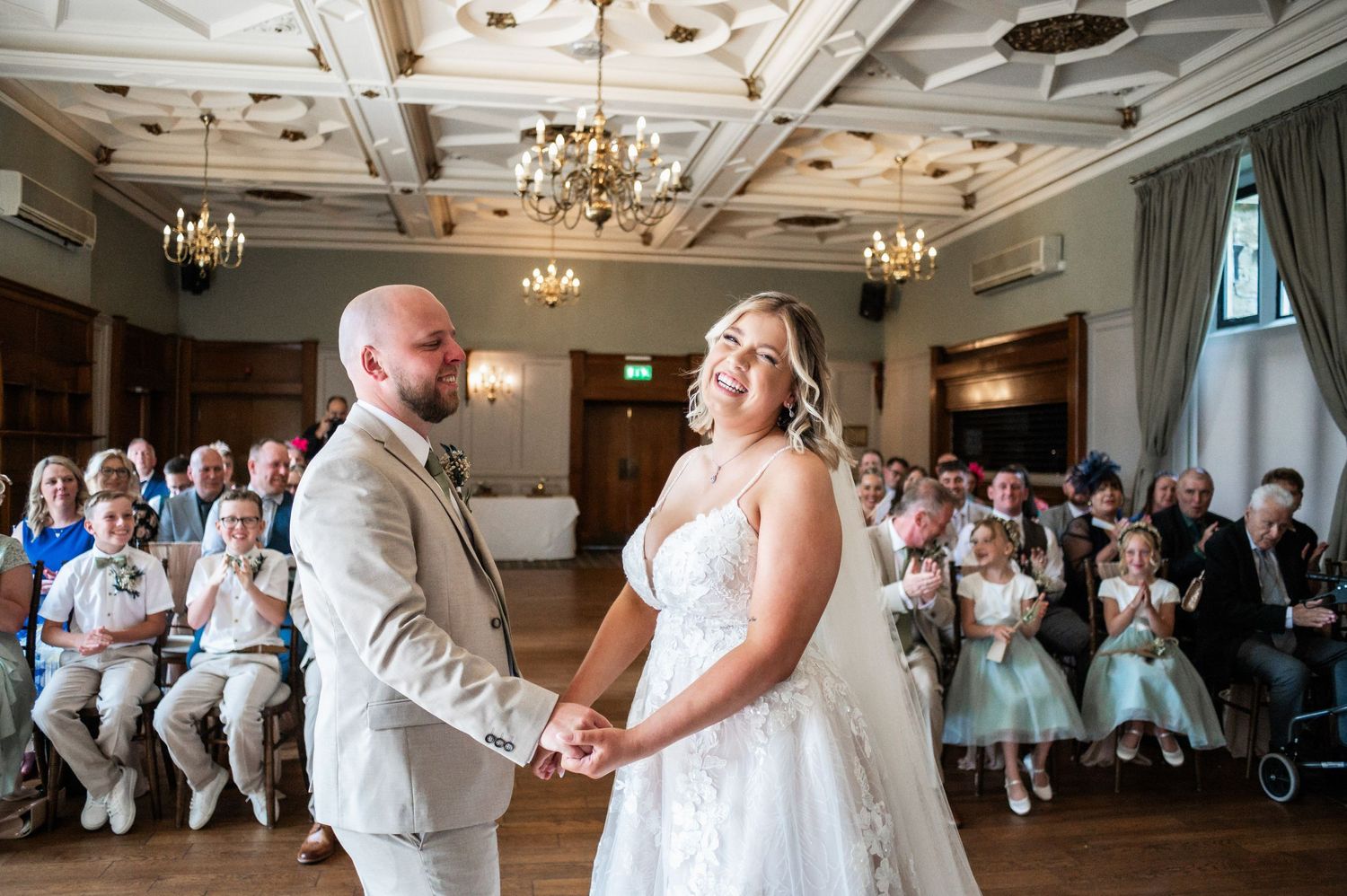 Wedding ceremony in an ornate ballroom with decorative ceiling and chandeliers.