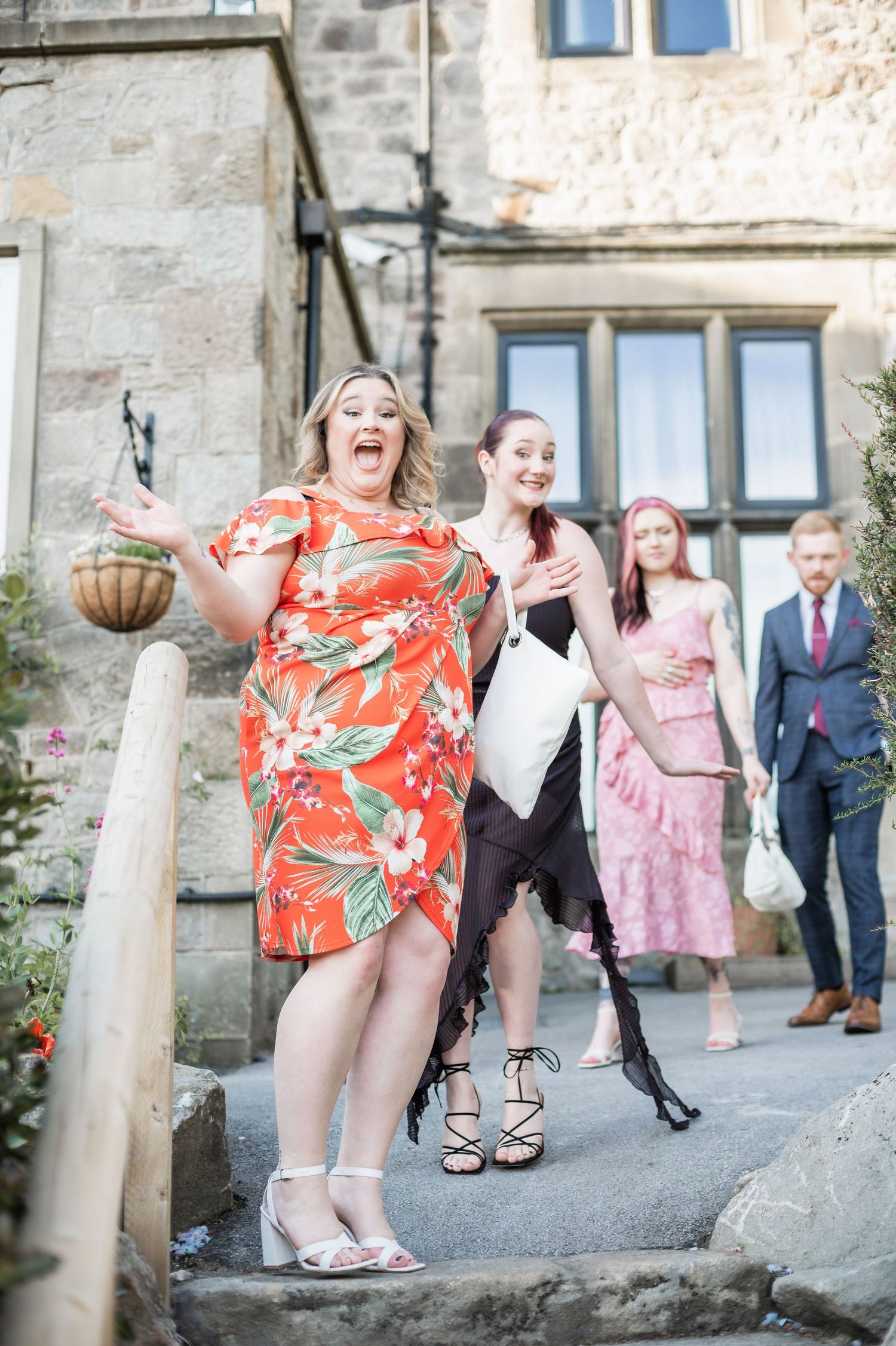 Wedding guests laugh joyfully outside historic stone building with hanging flower baskets.