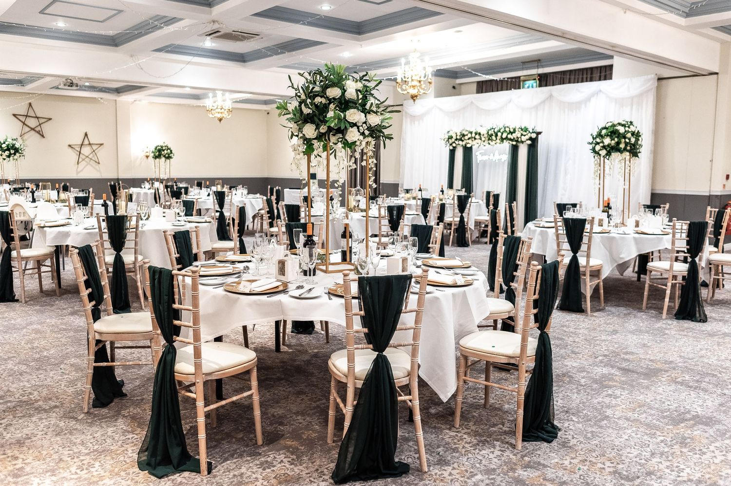 Elegant wedding reception venue with tall floral centerpieces and black chair sashes.