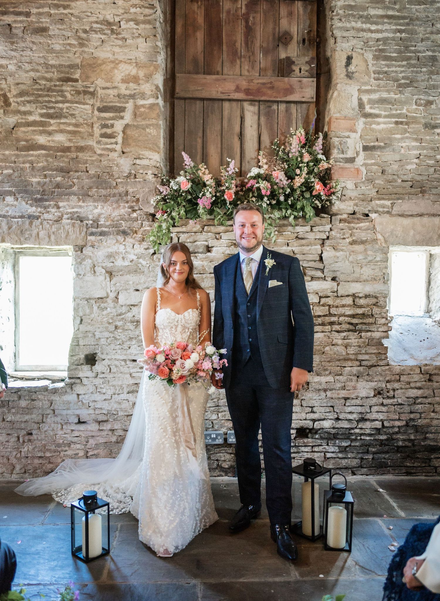Wedding couple poses in rustic stone venue with wooden door and floral arch.