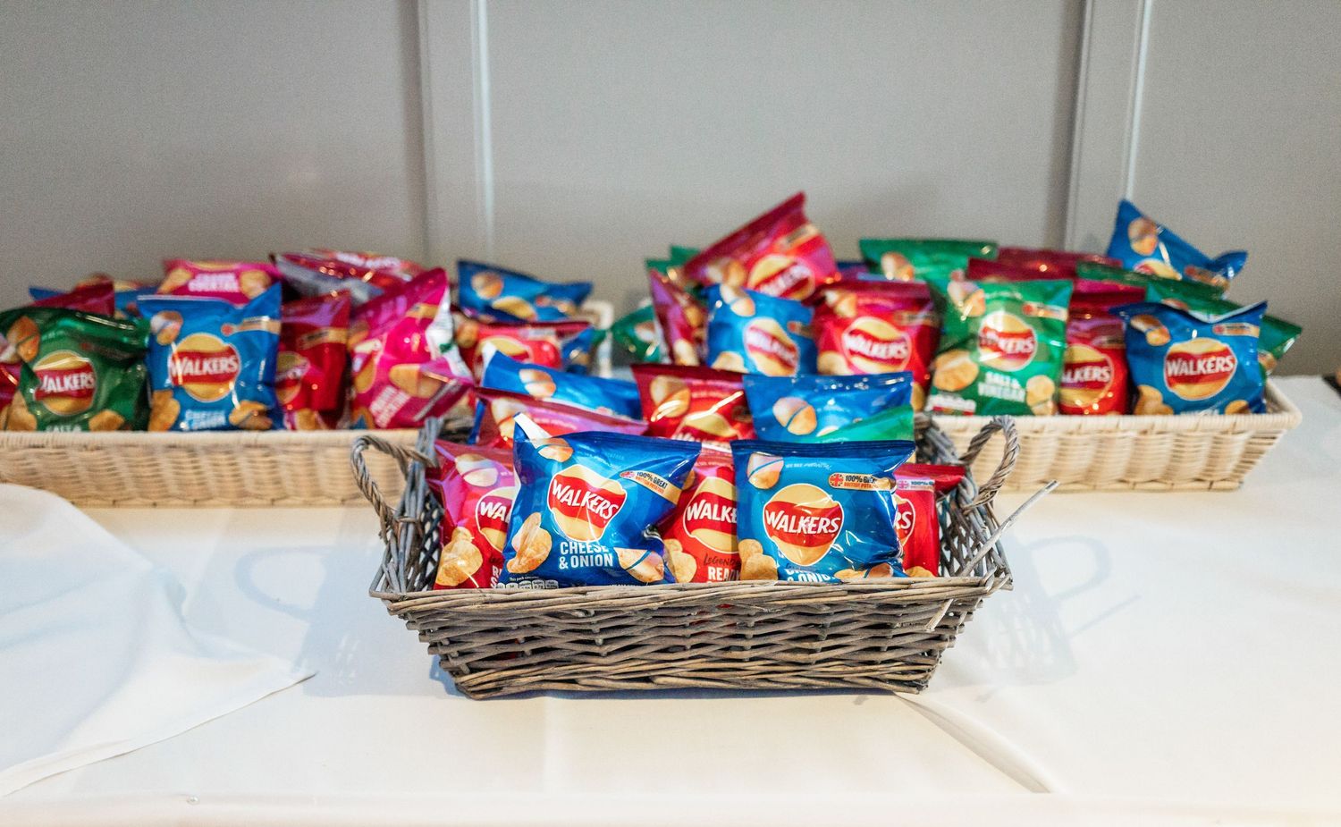 Colorful snack bags arranged in woven baskets on white tablecloth.