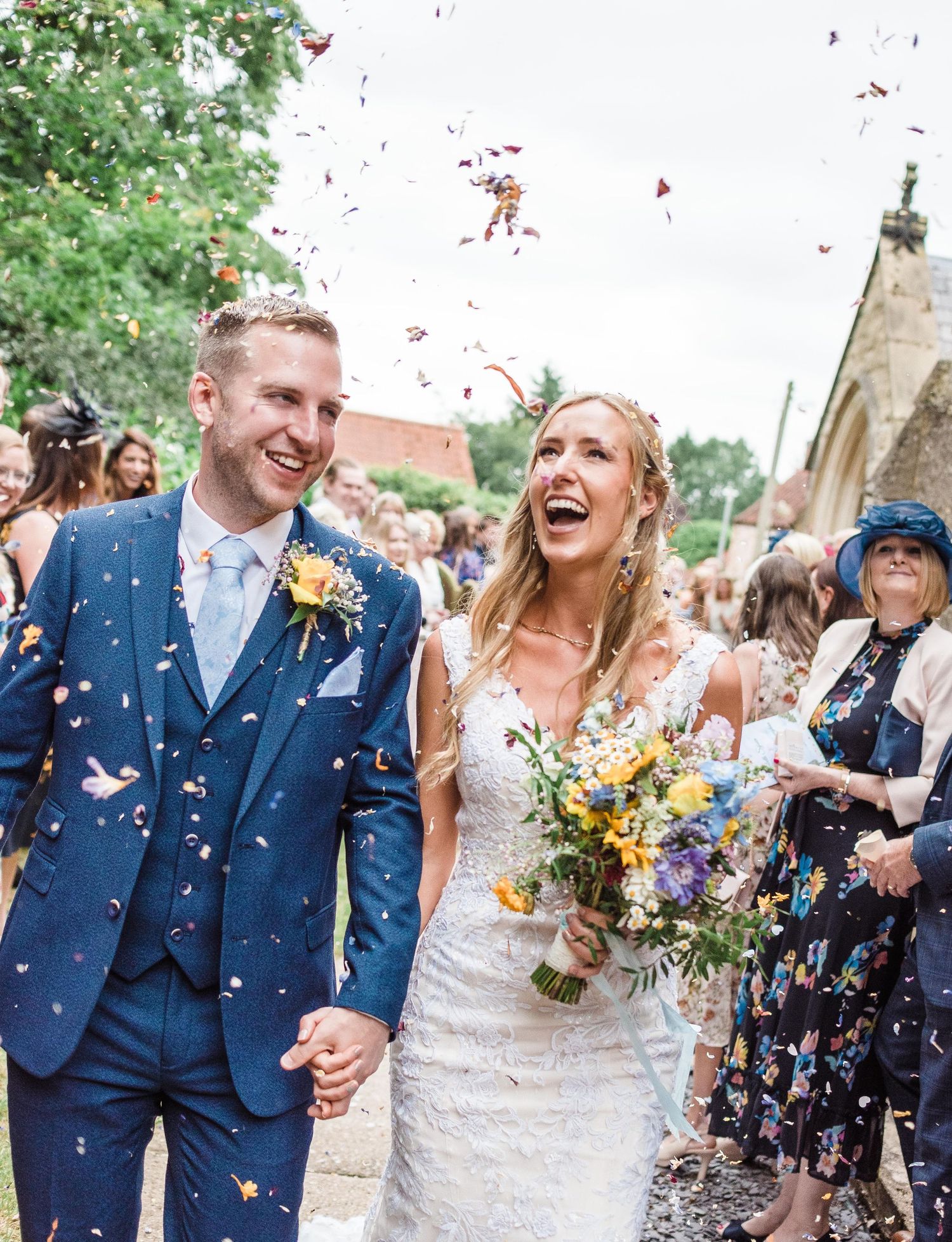 A joyful wedding celebration as the newlyweds exit their ceremony while guests shower them with red confetti petals.