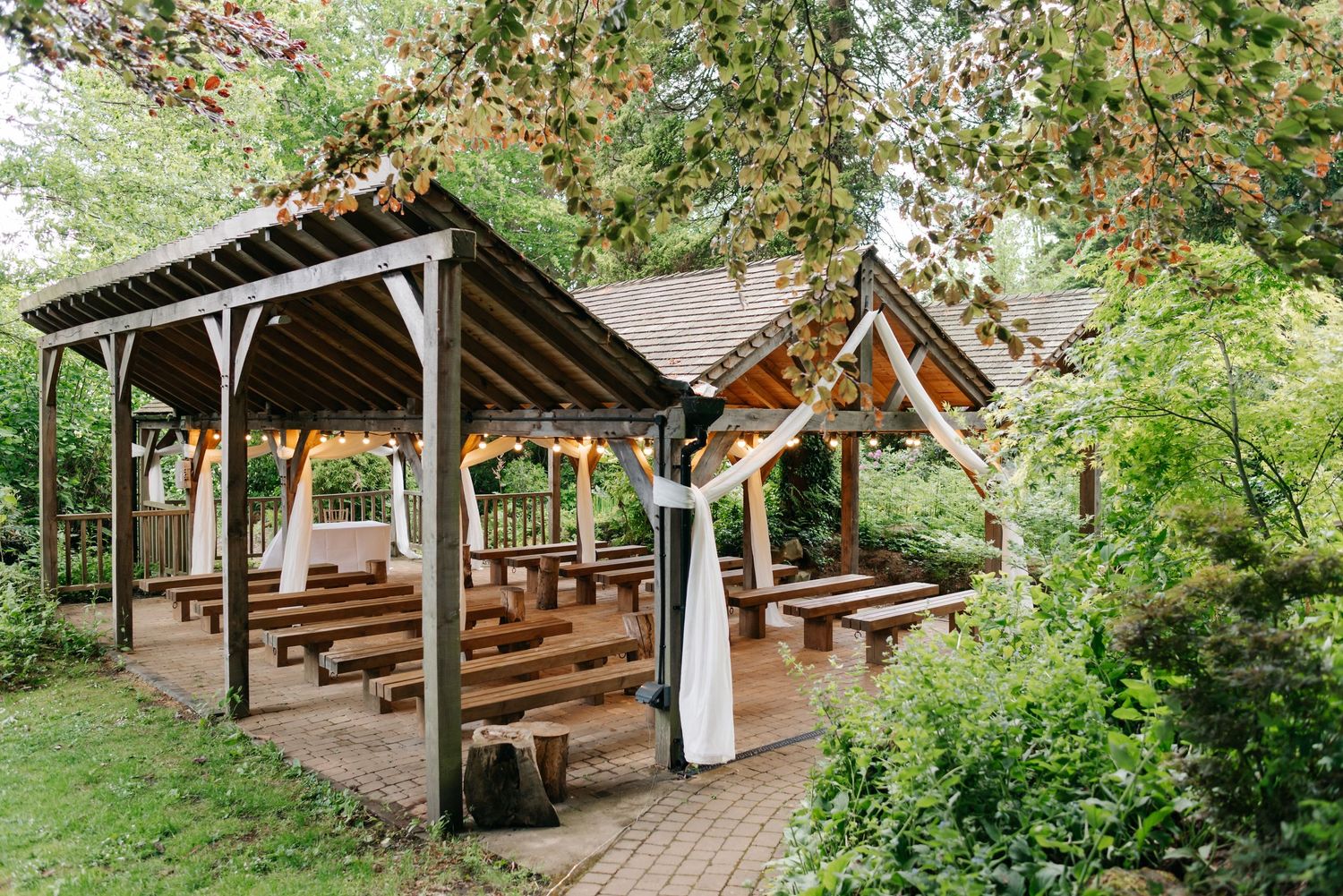 Rustic outdoor wooden ceremony space with benches surrounded by lush greenery and forest trees.