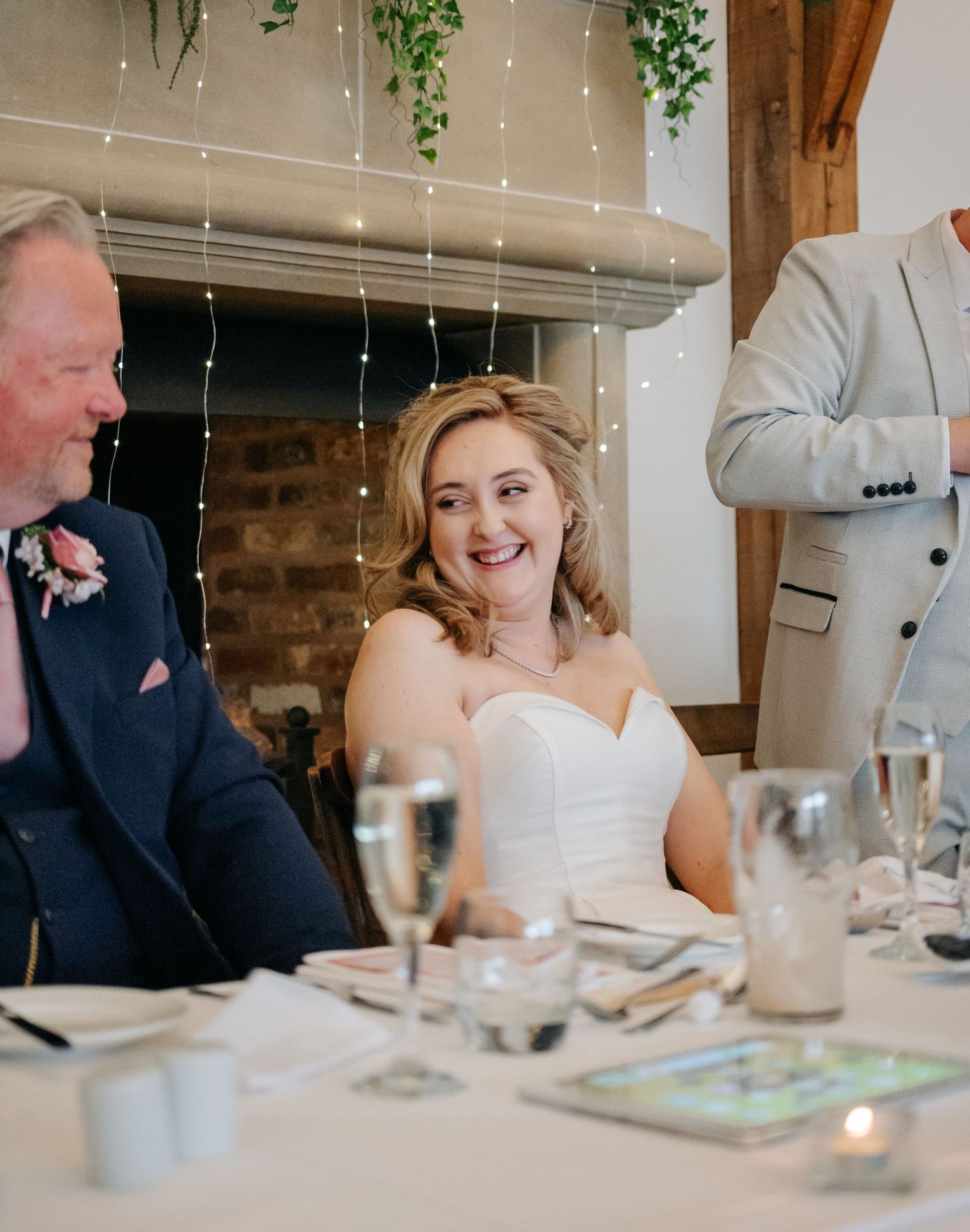 Candid reception moments captured at elegant table setting with fairy lights and brick backdrop.