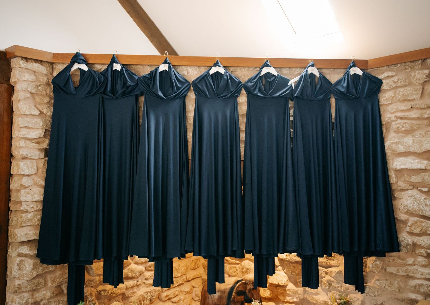 Row of black formal dresses hanging on hangers against stone wall in retail boutique setting.