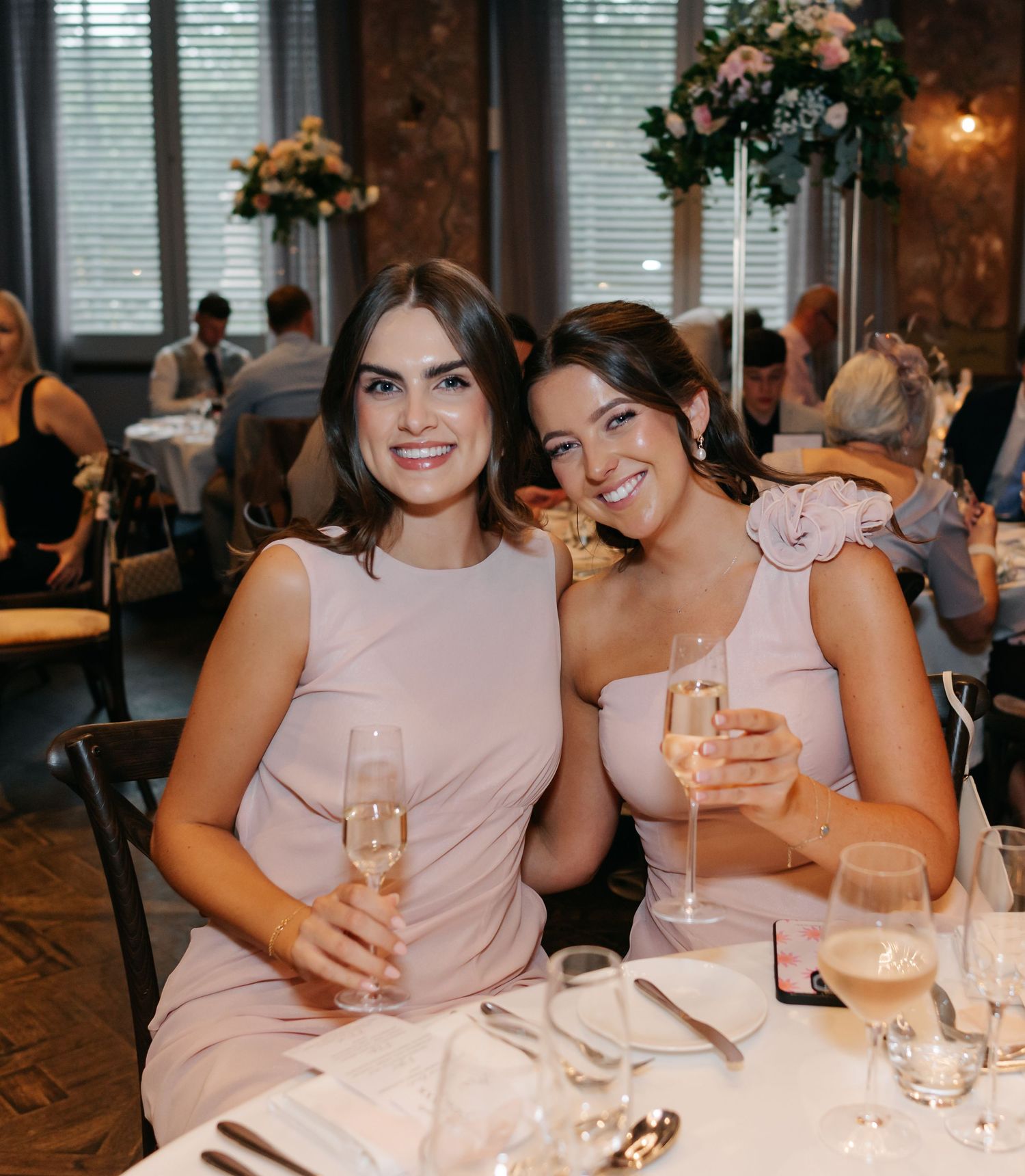Wedding party members in blush pink dresses enjoying champagne at a reception dinner.