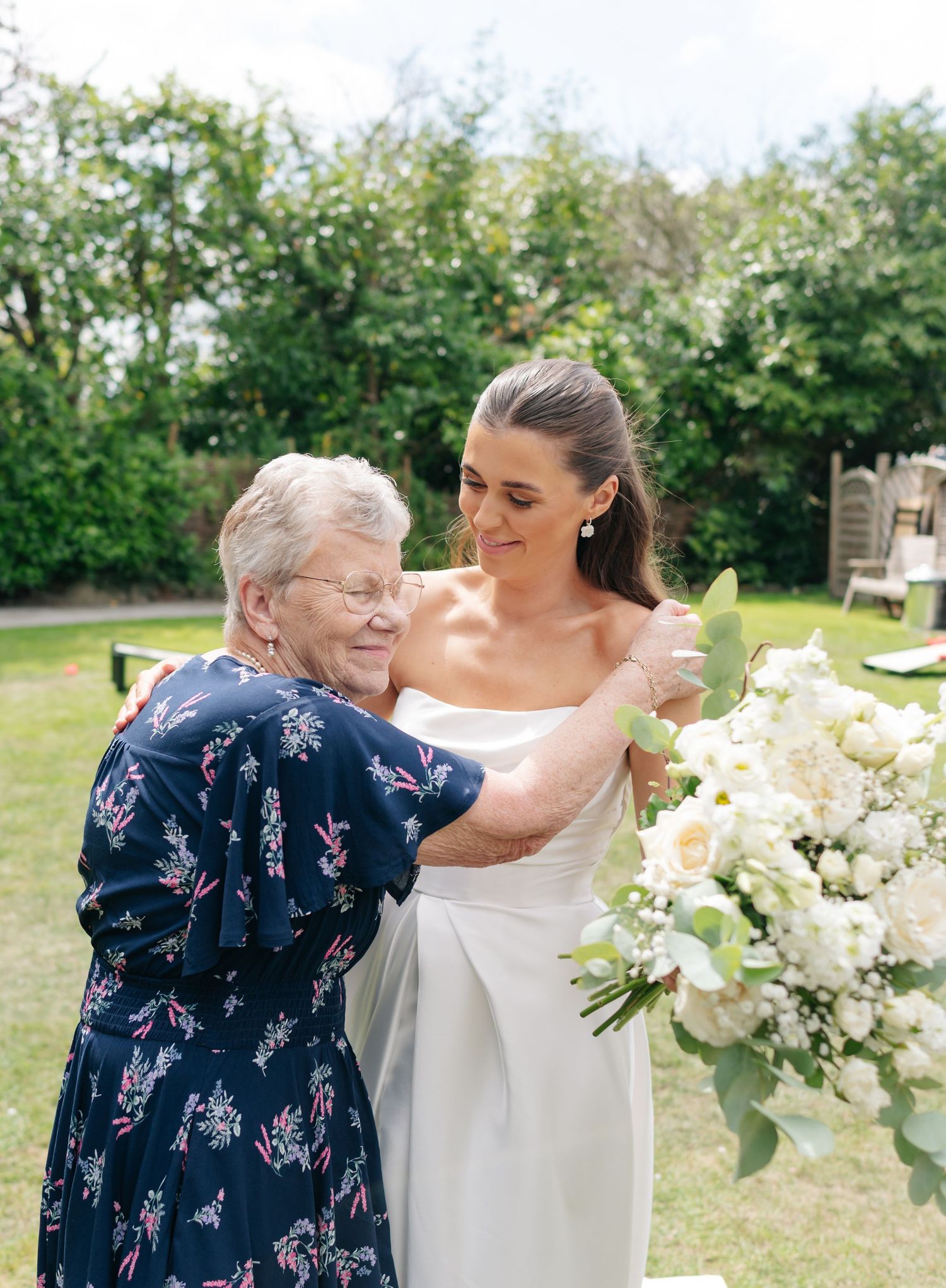 Emotional wedding moment with bride in white dress embracing someone in a floral navy dress.