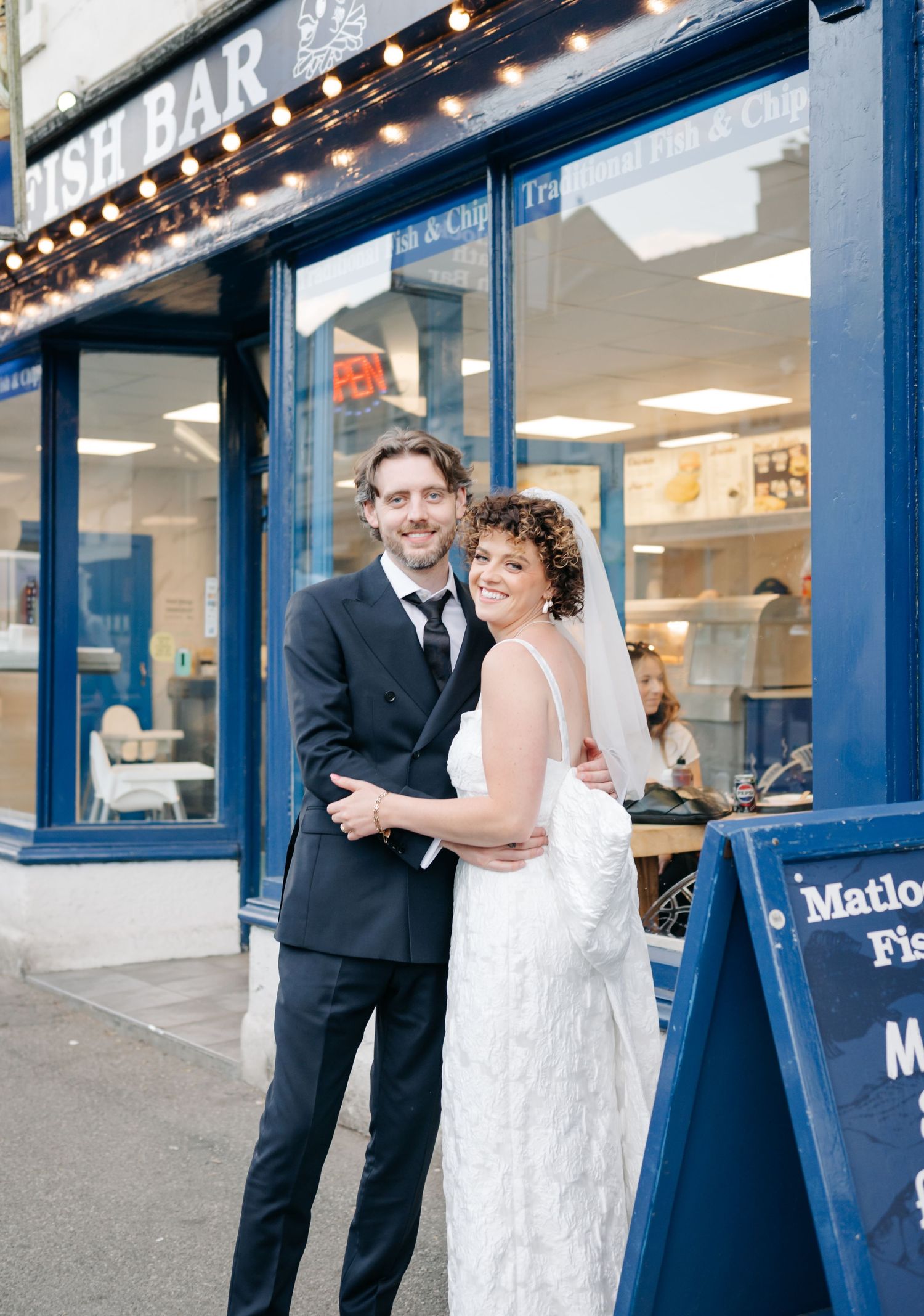 A couple shares a playful moment outside a storefront with blue trim.