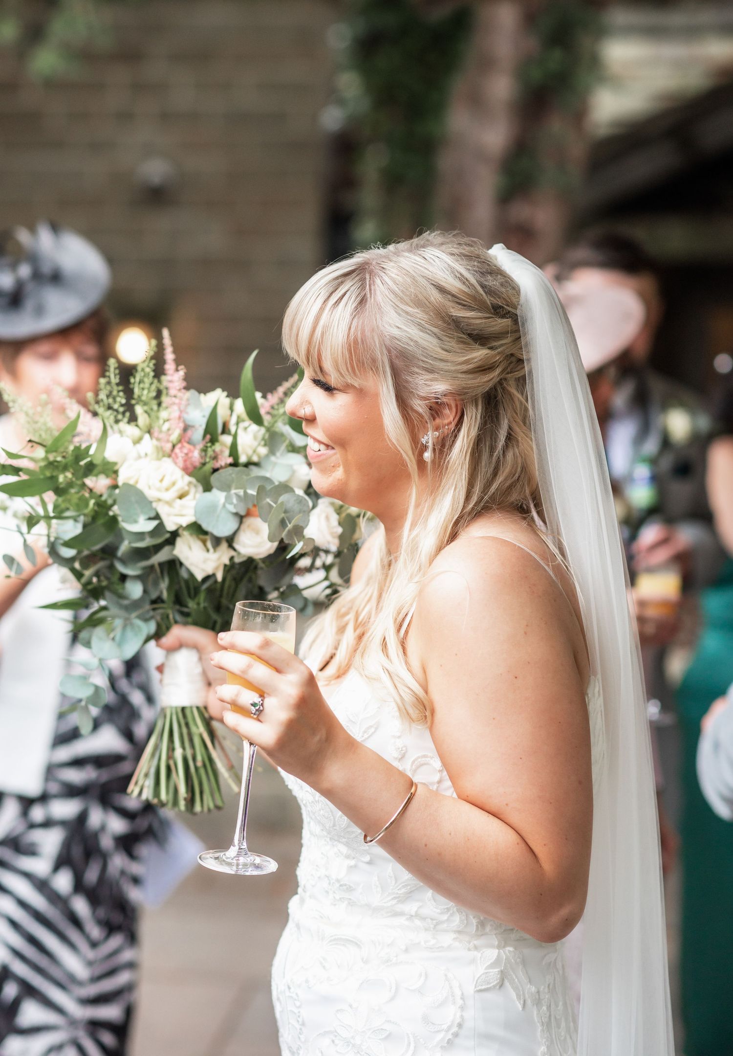 Bride in lace wedding dress holding champagne glass and beautiful bouquet with eucalyptus and roses.