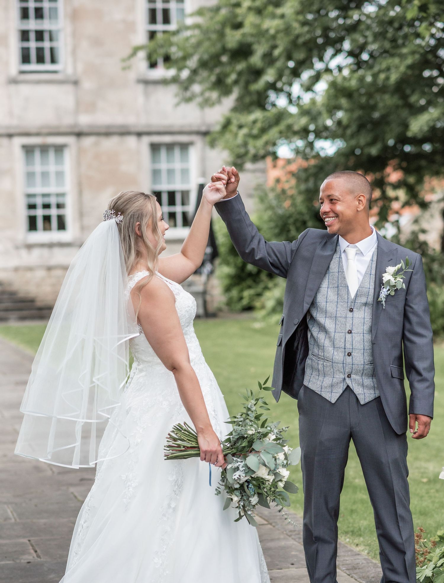 Newlyweds share joyful moment raising clasped hands in garden setting.
