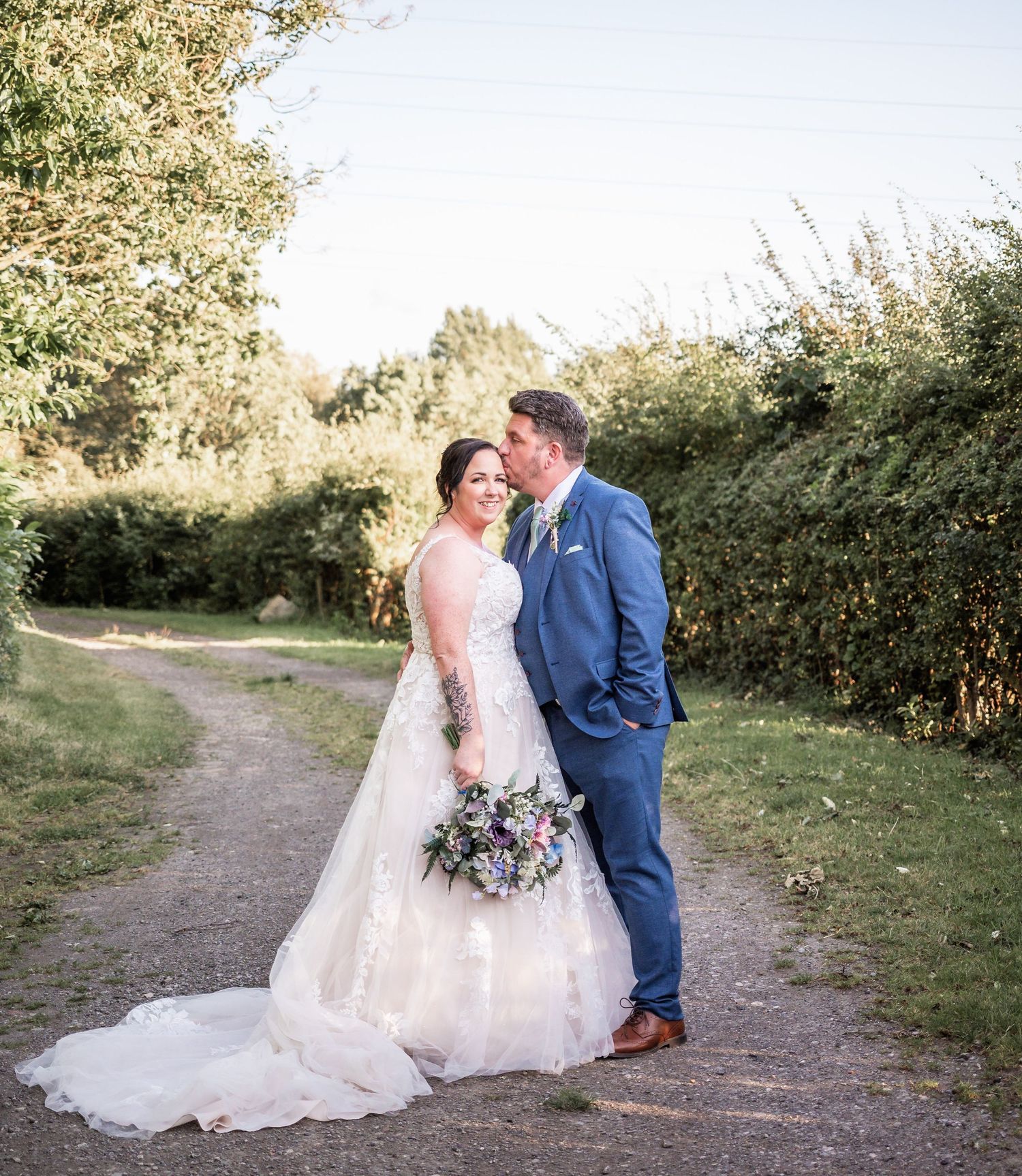 Newlyweds share romantic moment on garden path with natural greenery backdrop.