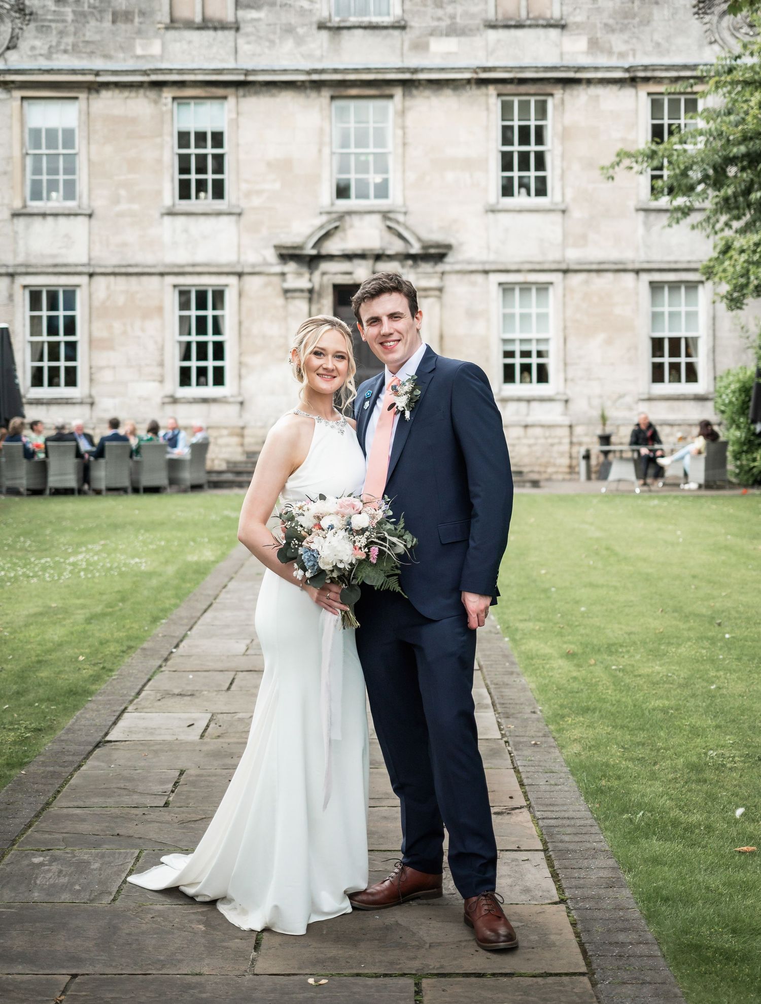 Newlyweds pose together on stone pathway in front of historic building.
