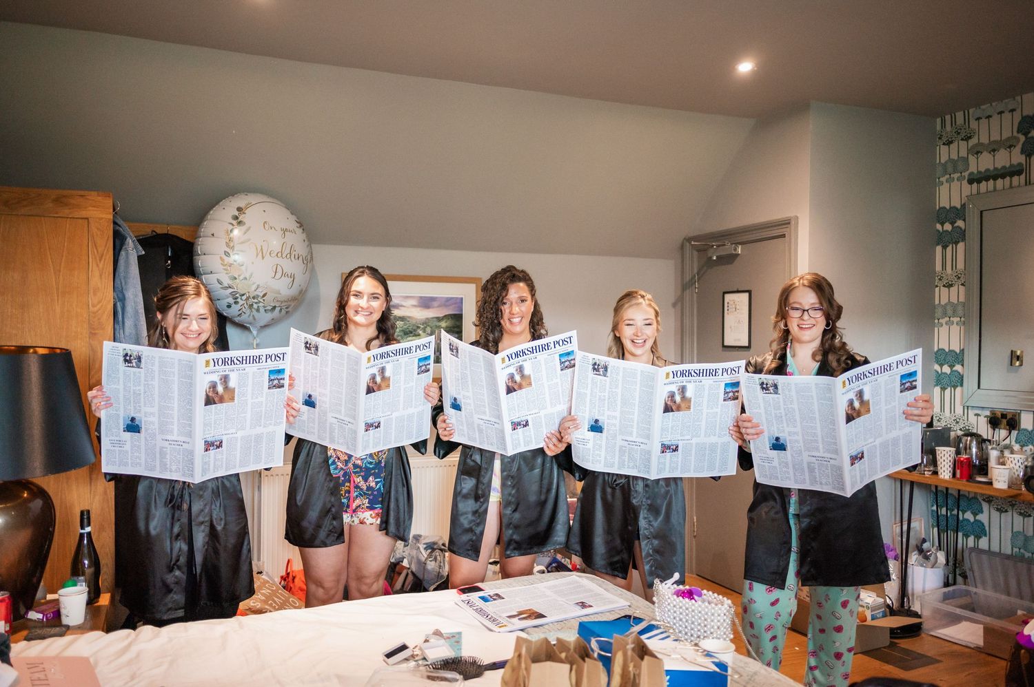 Group holding up decorative papers in preparation room during wedding festivities.
