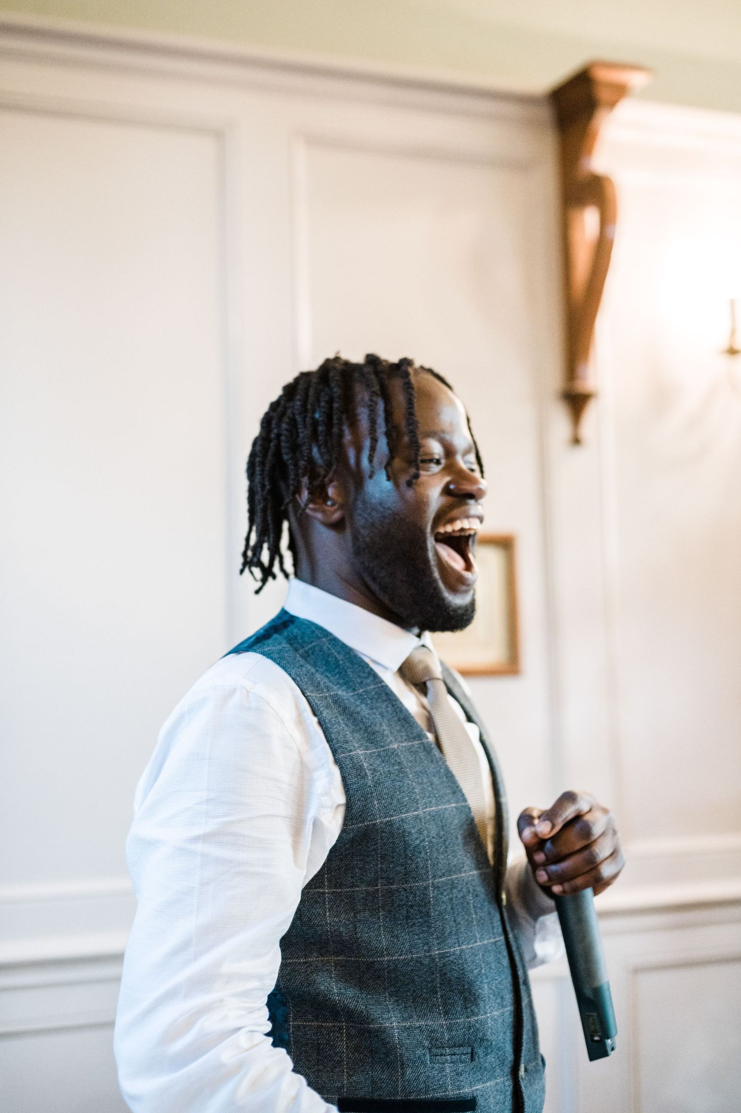 Person wearing grey vest and white shirt expressing joy while speaking at wedding reception.