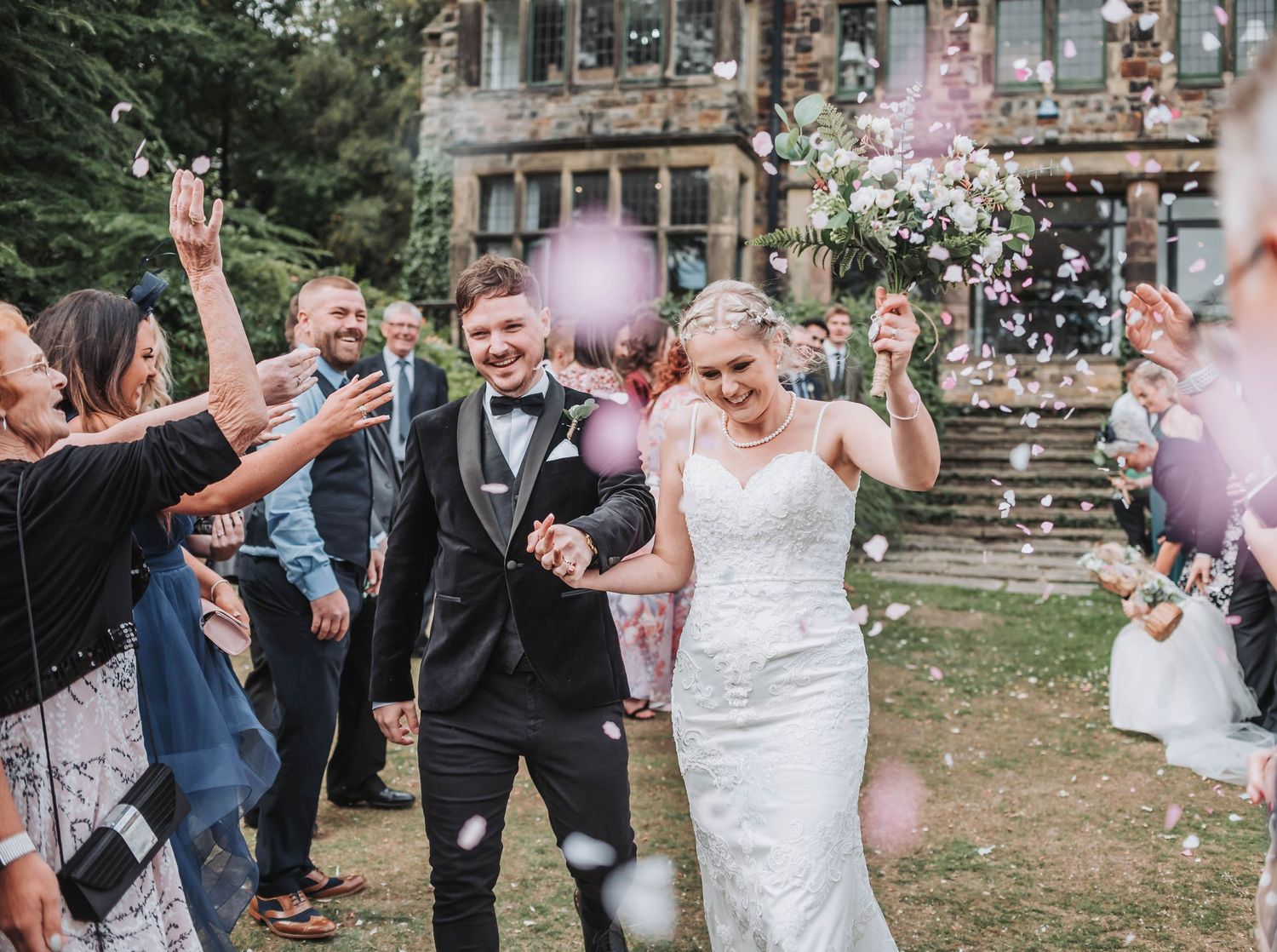 Celebration with confetti and balloons outside ornate stone building during wedding exit.