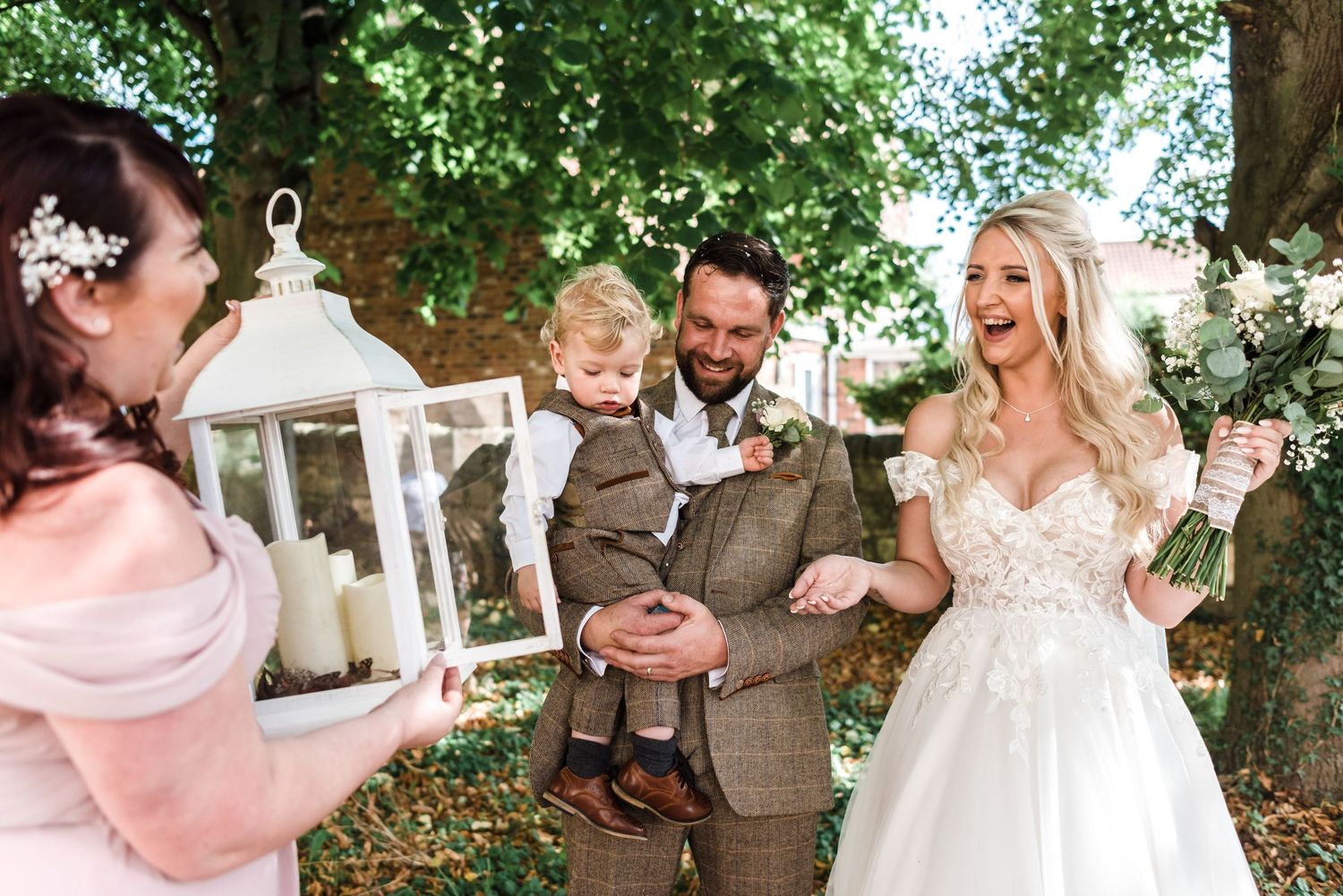Wedding couple holding young child with decorative lantern outdoors.