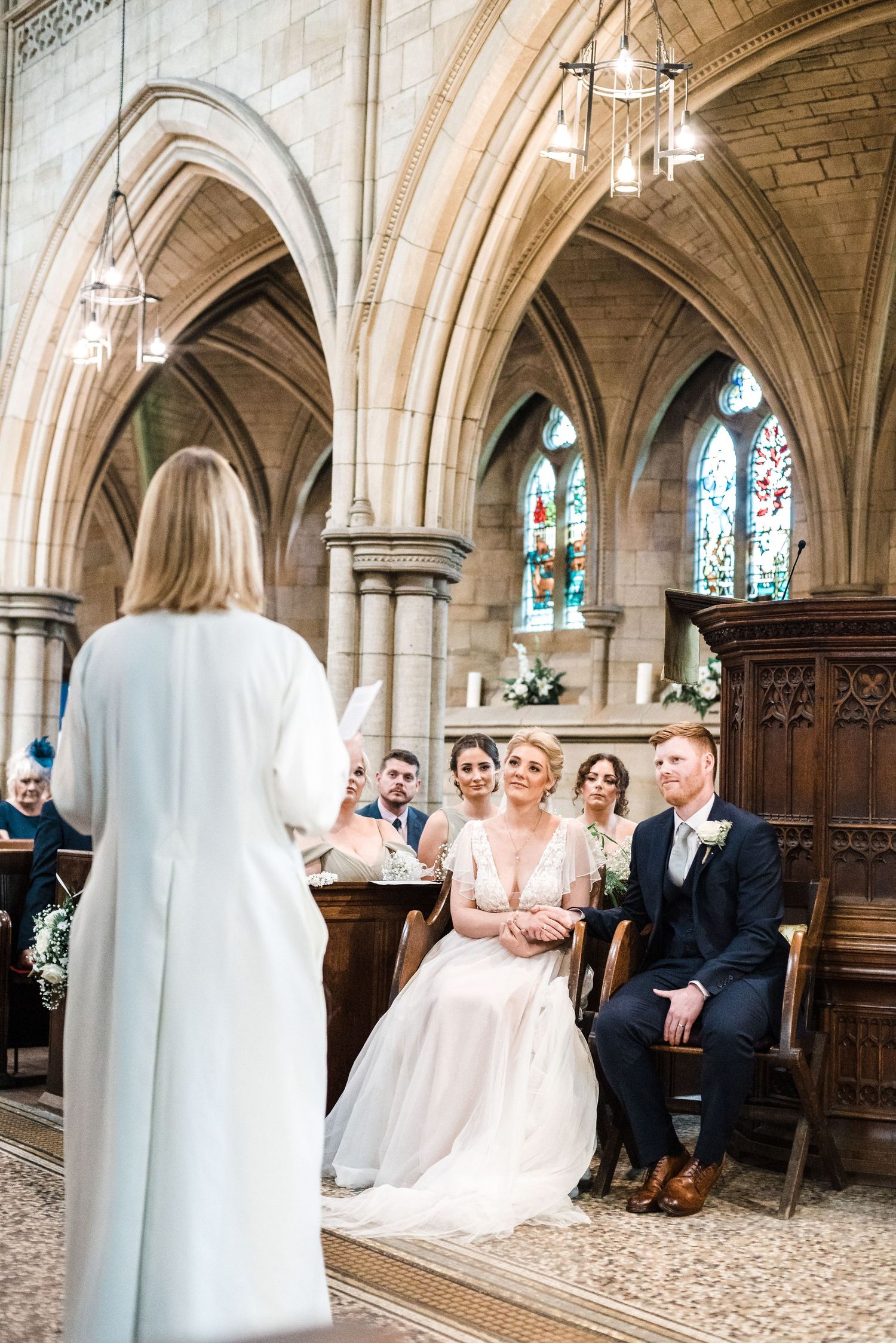 A church wedding ceremony with stone arches and stained glass windows in the background.
