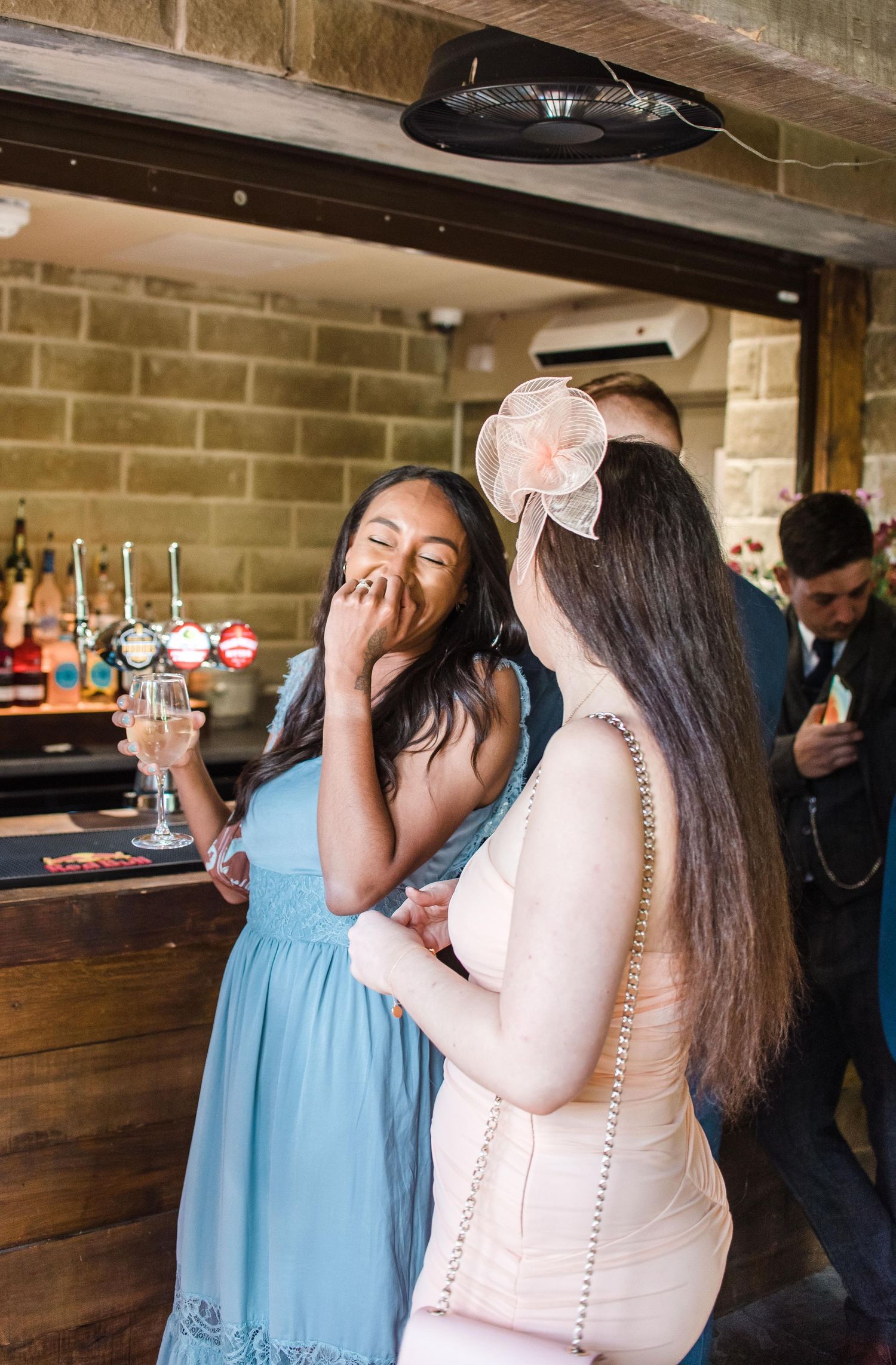 Wedding guests sharing laughs at rustic wooden bar during reception.