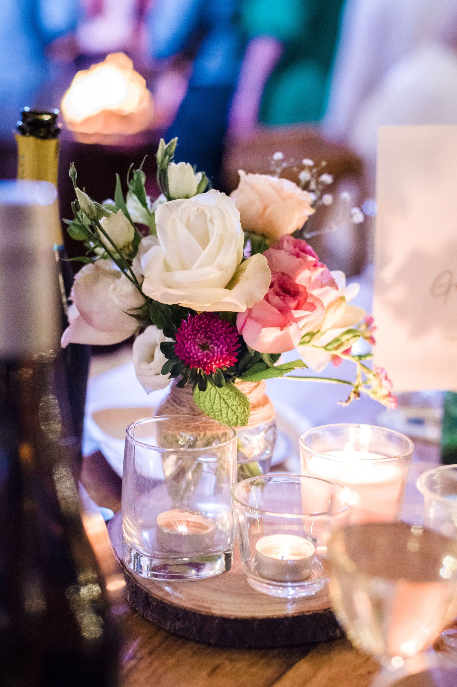 Elegant wedding centerpiece with white and pink roses in a mason jar surrounded by glowing candles.