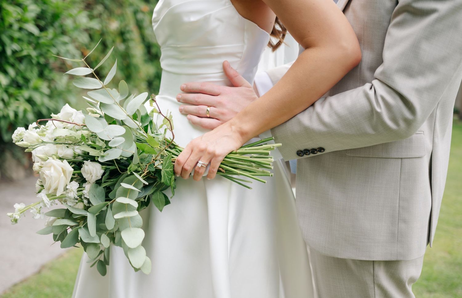 Wedding party holding elegant white and green floral bouquets outdoors.