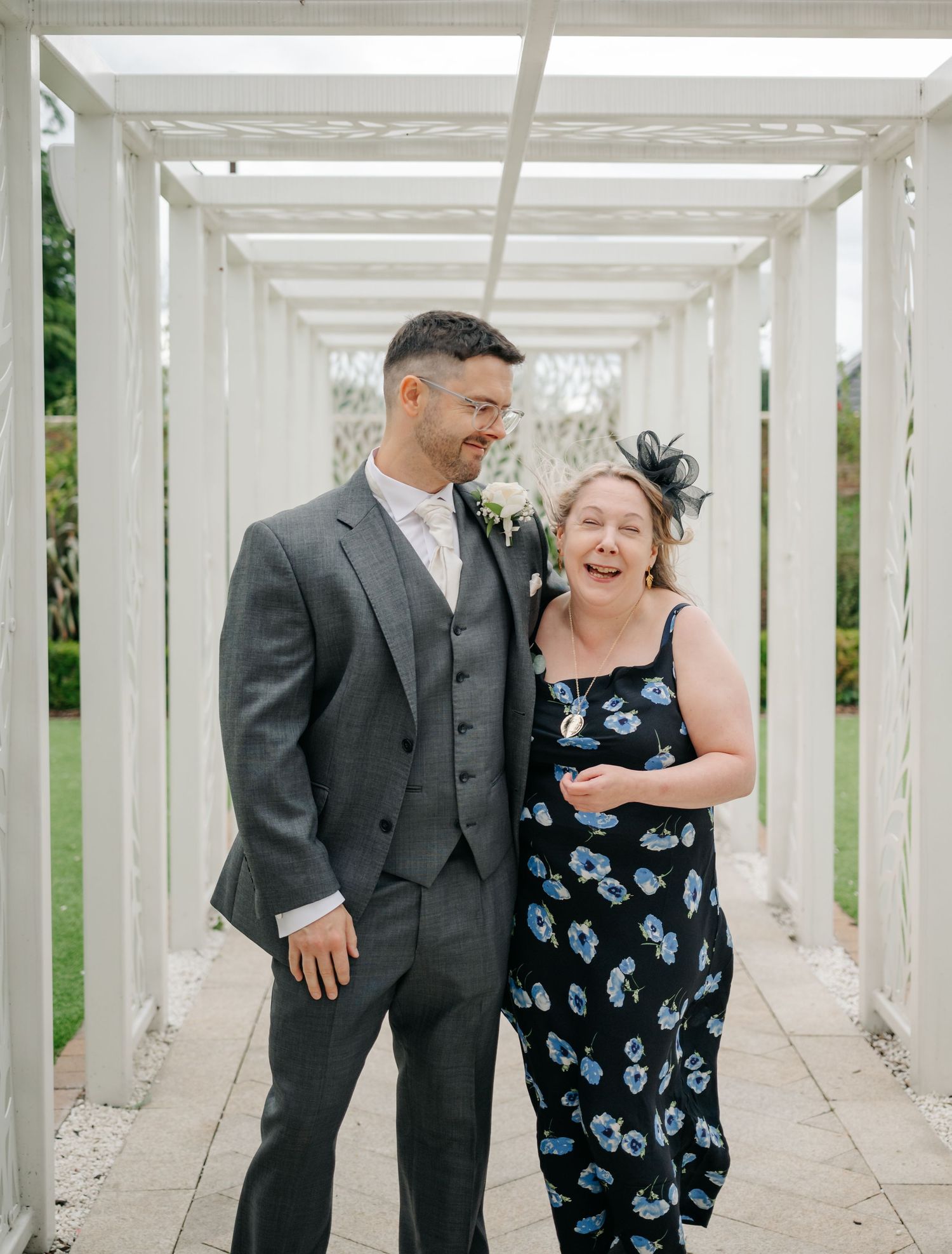 A couple shares a joyful candid moment together under a white pergola walkway.