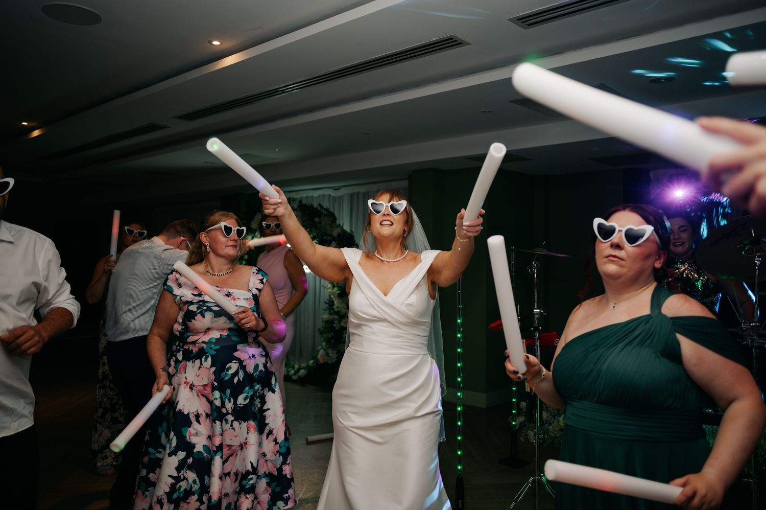 Wedding guests dance with light-up foam sticks at a reception party.