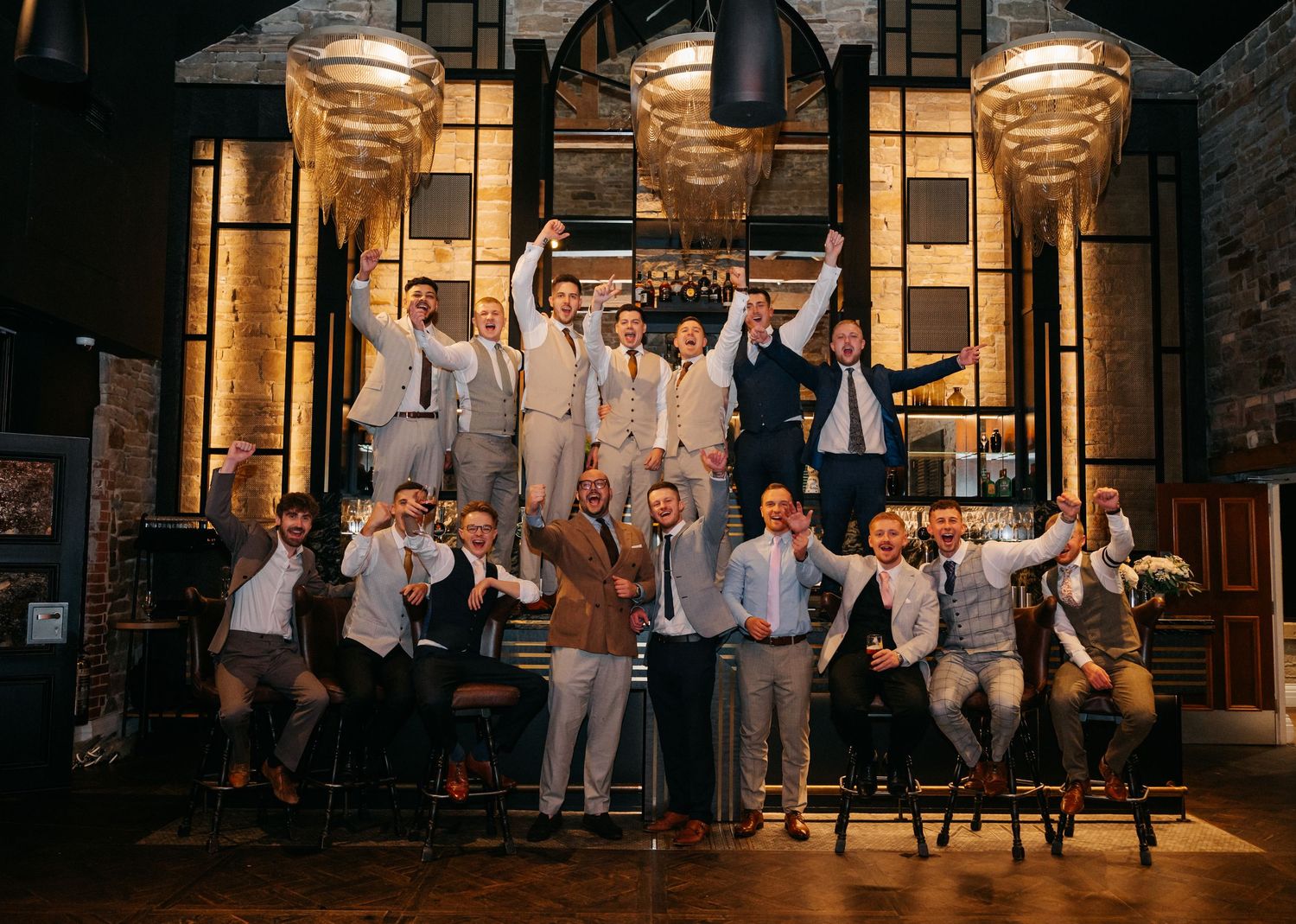 Wedding party celebrates with joyful jumping photo in front of illuminated building at night.