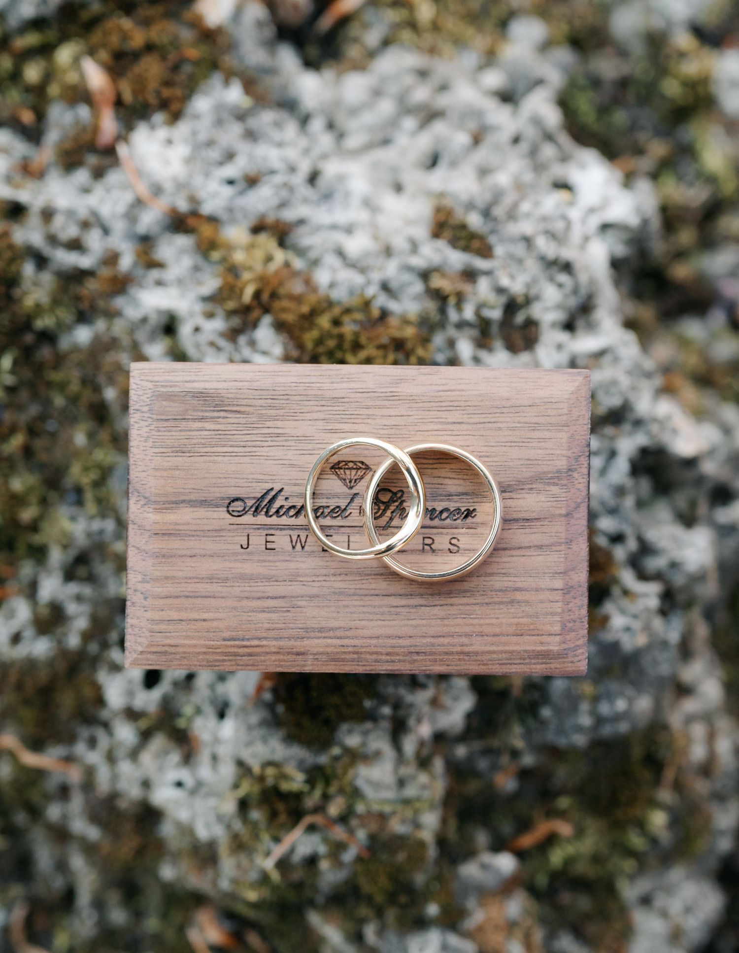 Wedding rings displayed on rustic wooden blocks with moss and natural textures in the background.