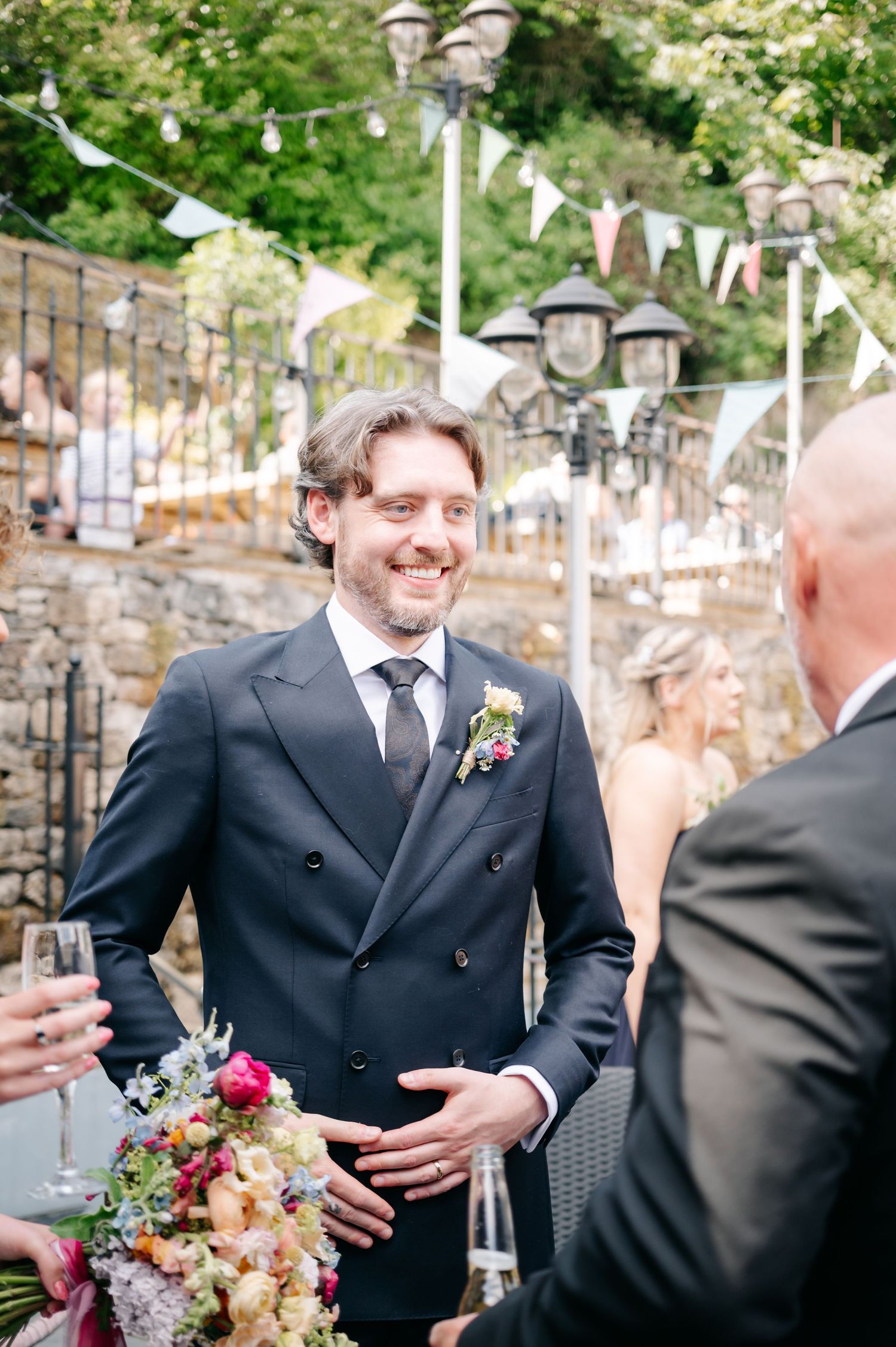 Wedding party mingles outdoors under white bunting decorations.