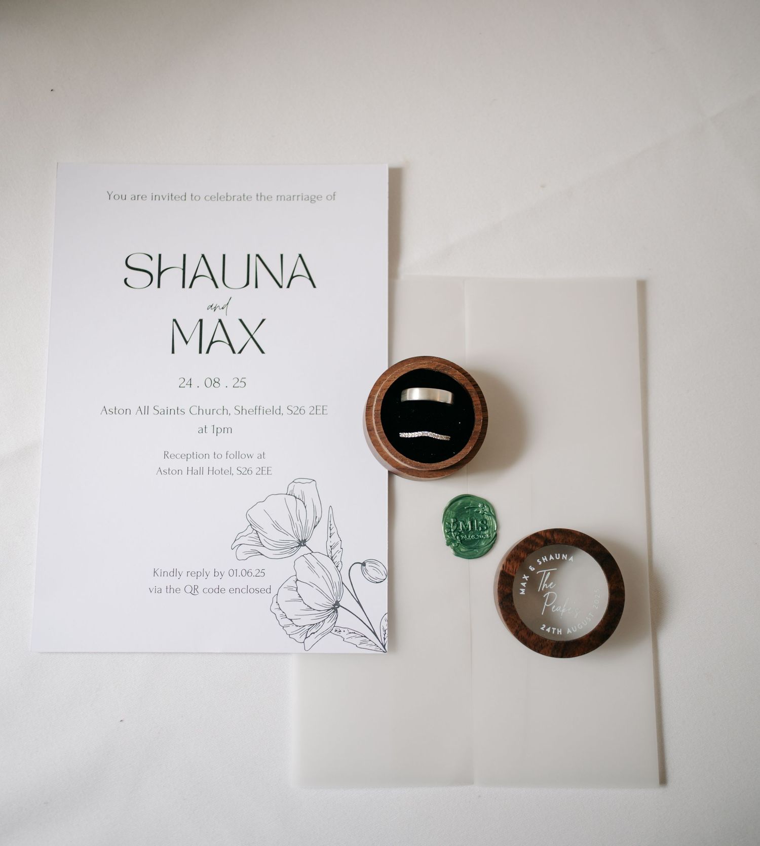 Simple white wedding invitation cards with floral designs and metallic round wax seals arranged on a light surface.