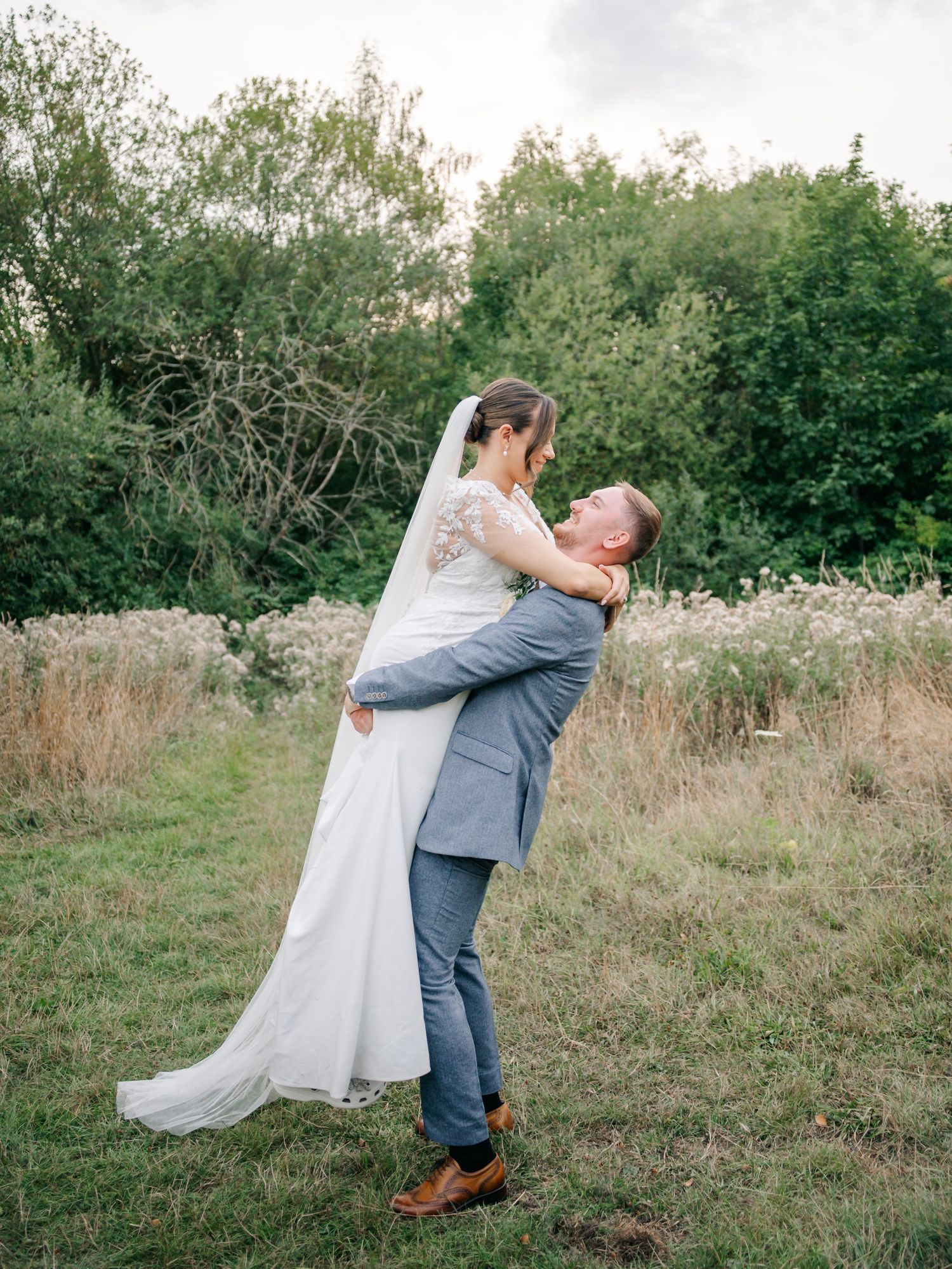 A couple embraces in a romantic lift pose against a natural outdoor backdrop.