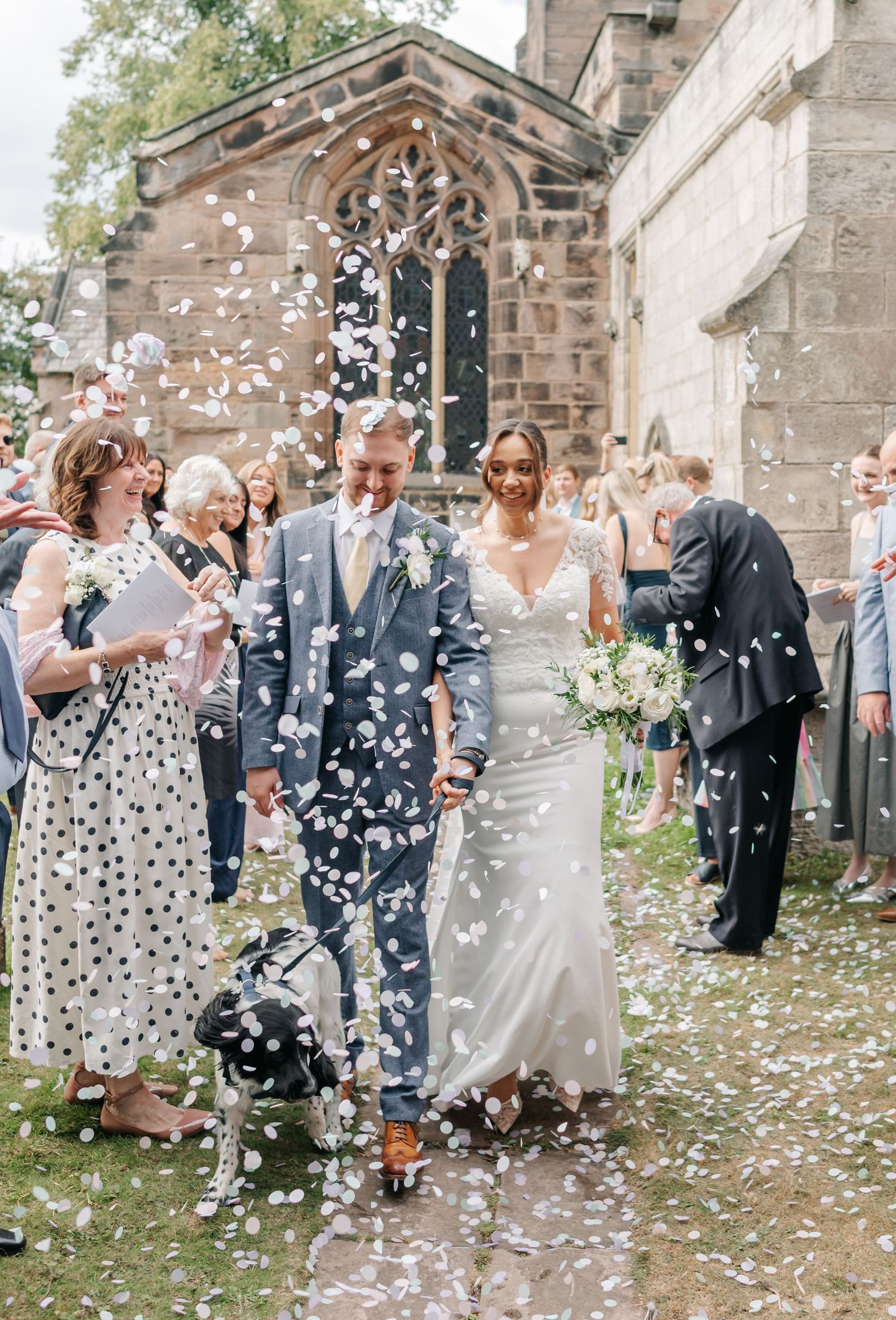 Wedding guests shower the newlyweds with confetti outside a stone church.