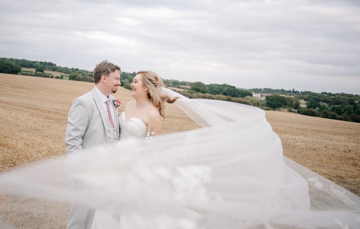 Wedding couple embraces in golden wheat field under cloudy sky.