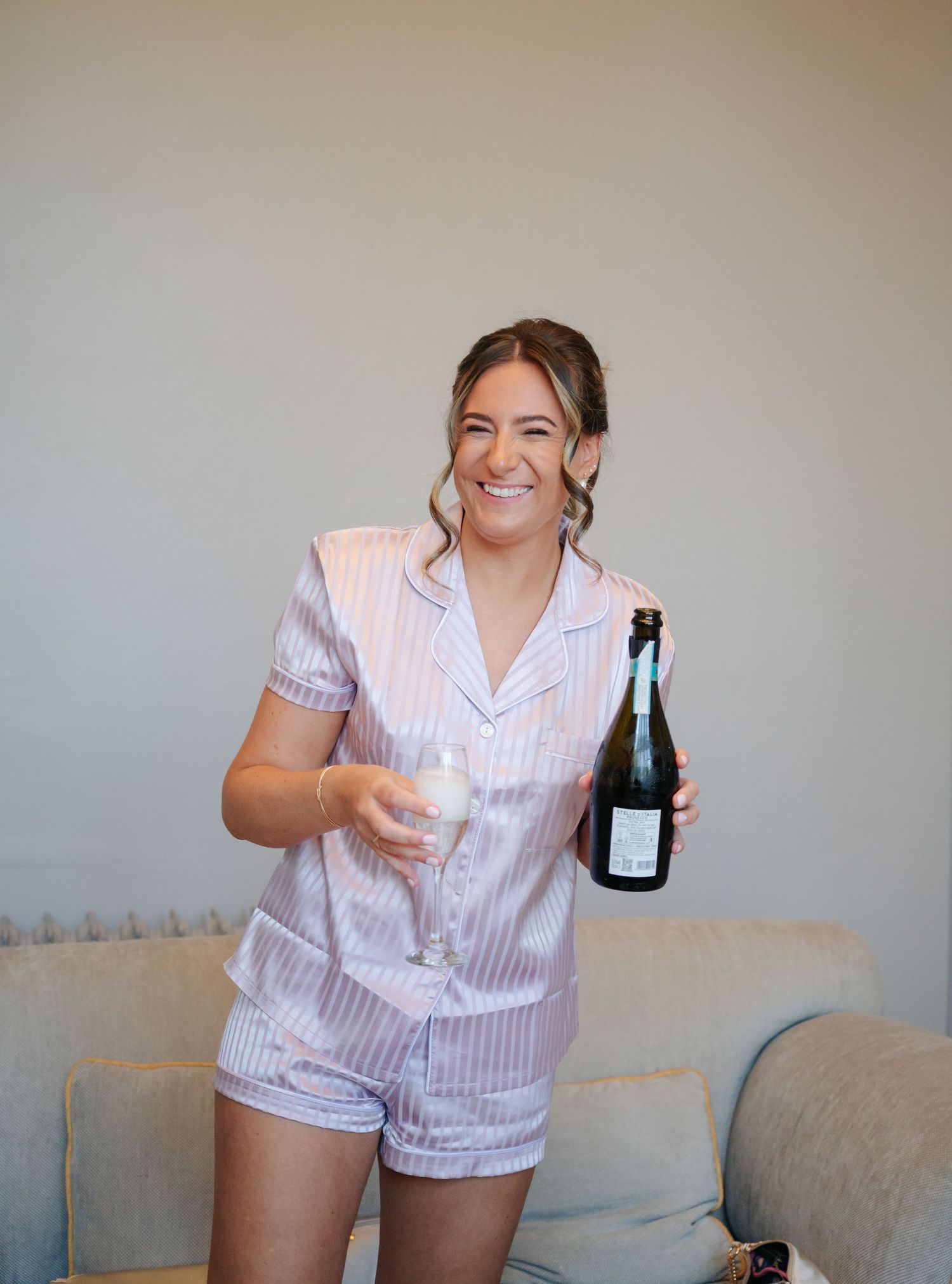 Someone wearing pink striped pajamas sits on a grey couch holding beverages.